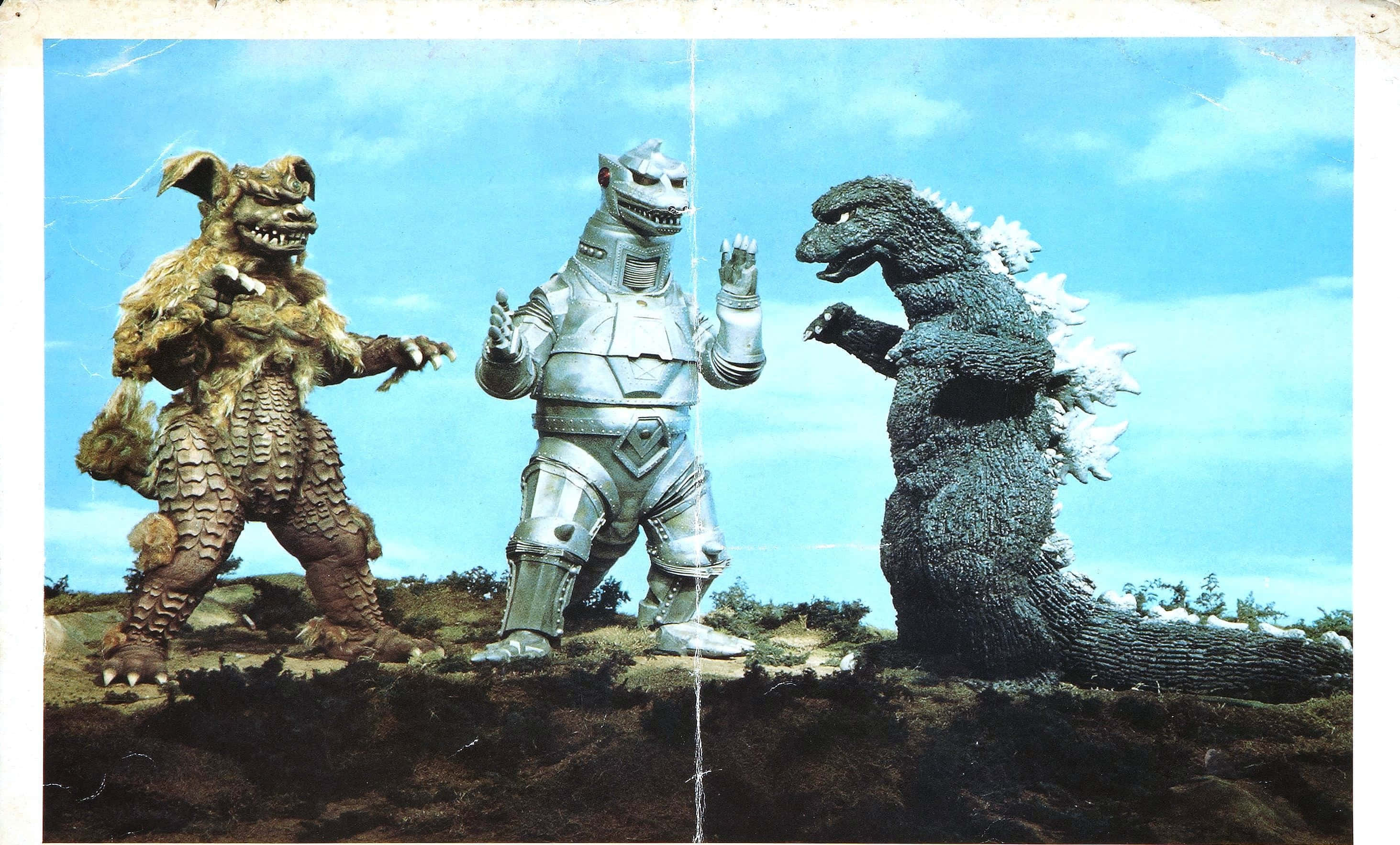 Robot Godzilla 桌布 壁紙 — 三隻巨型怪獸站在荒蕪的山坡上，天空湛藍，白雲點點。
