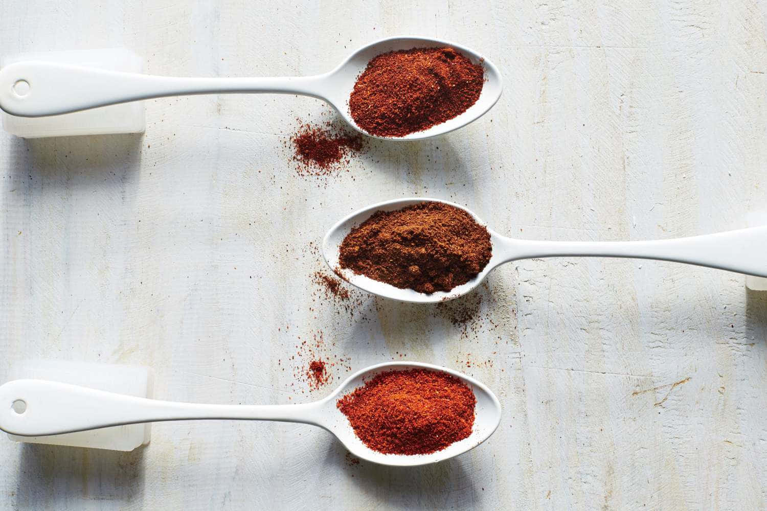 Red Chili Powder 桌布 壁紙 — 三隻白色湯匙盛載著鮮紅色香料，置於有紋理的白色木質表面上。