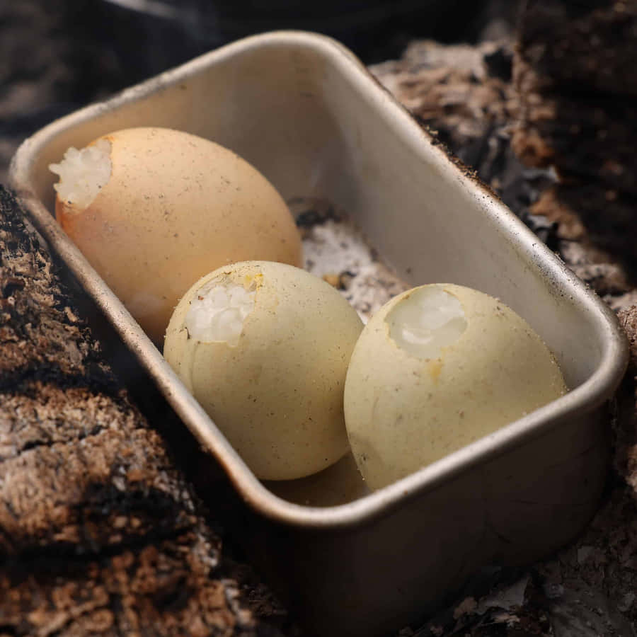 Eggshell 桌布 壁紙 — 三隻蛋殼破裂的雞蛋放在一個金屬托盤中，托盤置於悶燒的灰燼和燒焦的木頭之間。