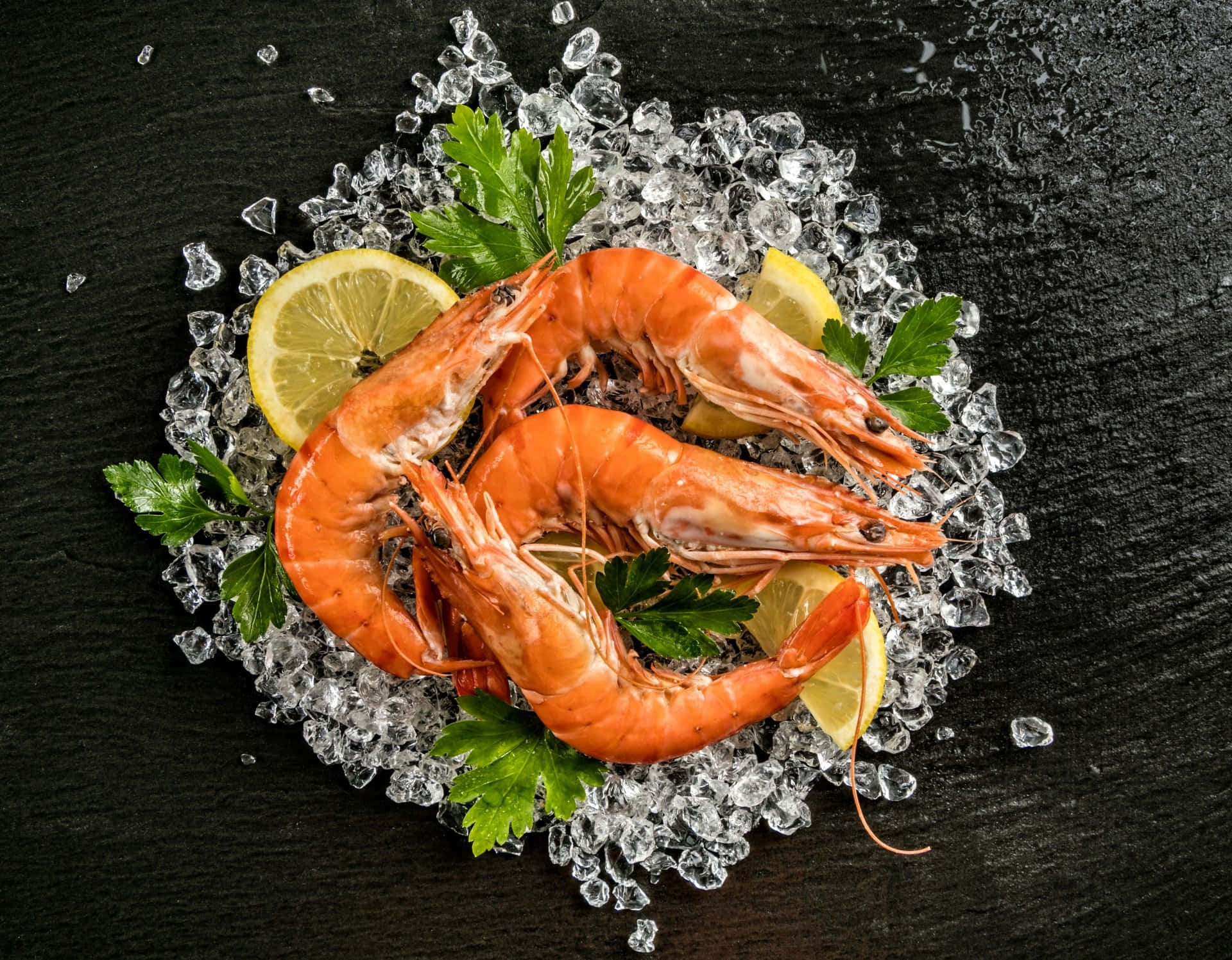 Seafood 桌布 壁紙 — 三隻鮮橙色熟蝦放在碎冰上，配以檸檬片和歐芹，置於深色石板表面。