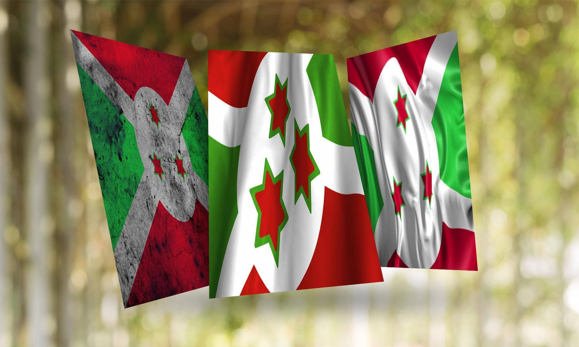 Burundi 桌布 壁紙 — 三面布隆迪國旗，帶有紅、綠、白顏色和紅色星星，在陽光明媚的森林中飄揚，背景有模糊的樹幹。