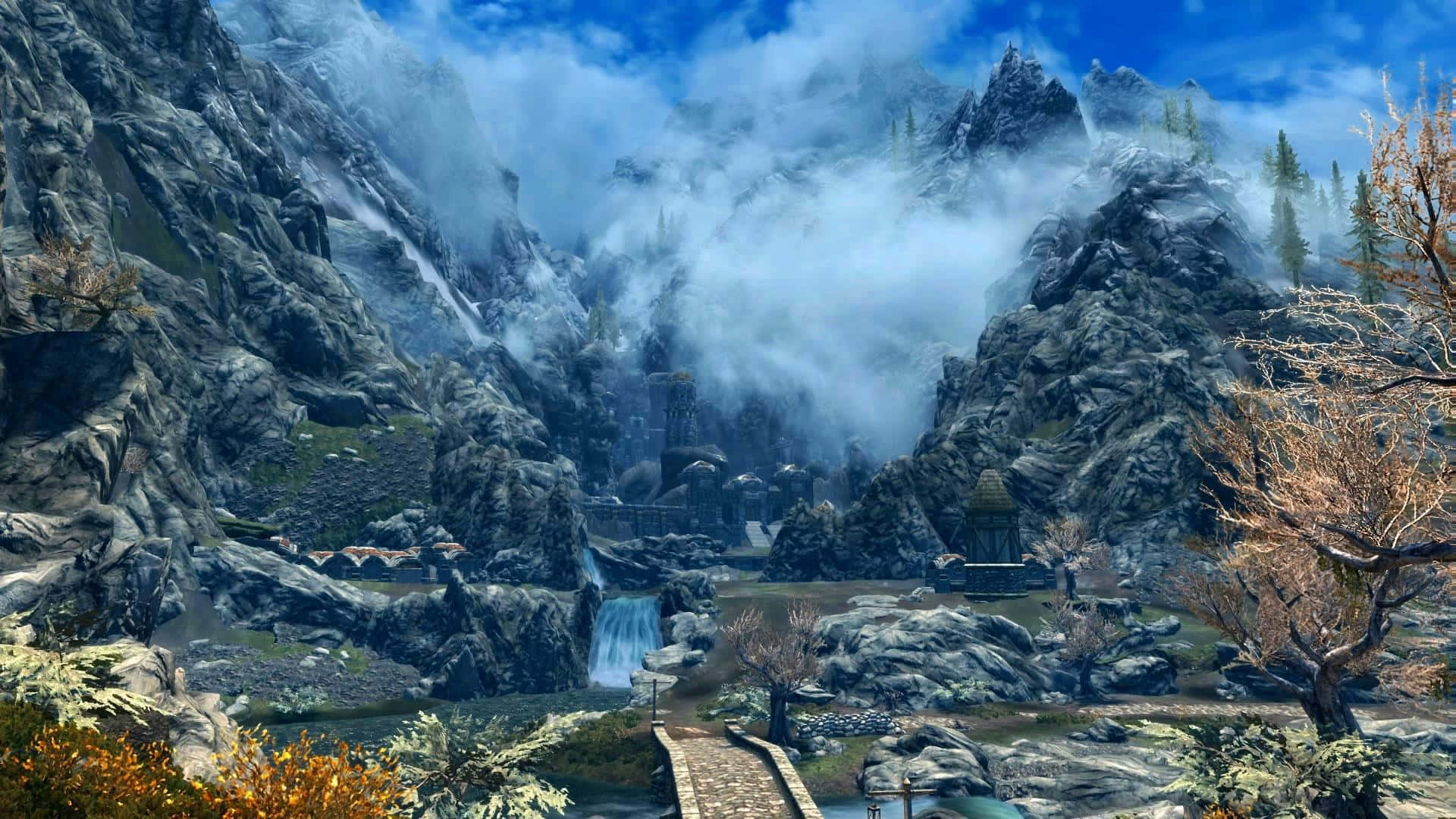 《上古卷軸V：天際》馬克塔爾的壯麗風景 壁紙 — 一個霧氣瀰漫的山谷，有古老的石頭廢墟、層疊的瀑布和秋樹，在明亮的藍天下。