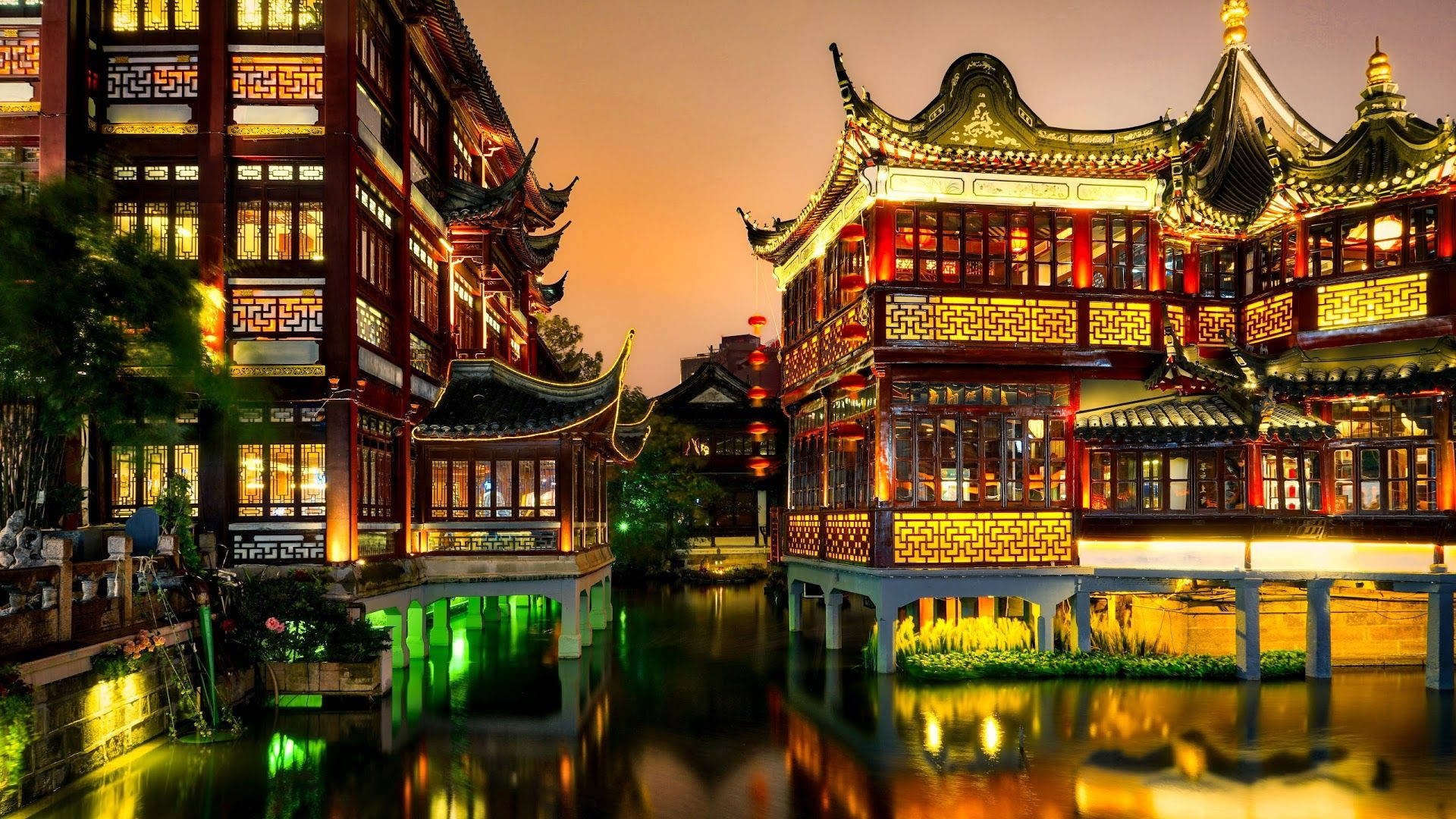 上海傳統園林 壁紙 — 傳統中式建築在黃昏時分溫暖地發光，其精緻的屋頂和燈籠倒映在寧靜的運河中。