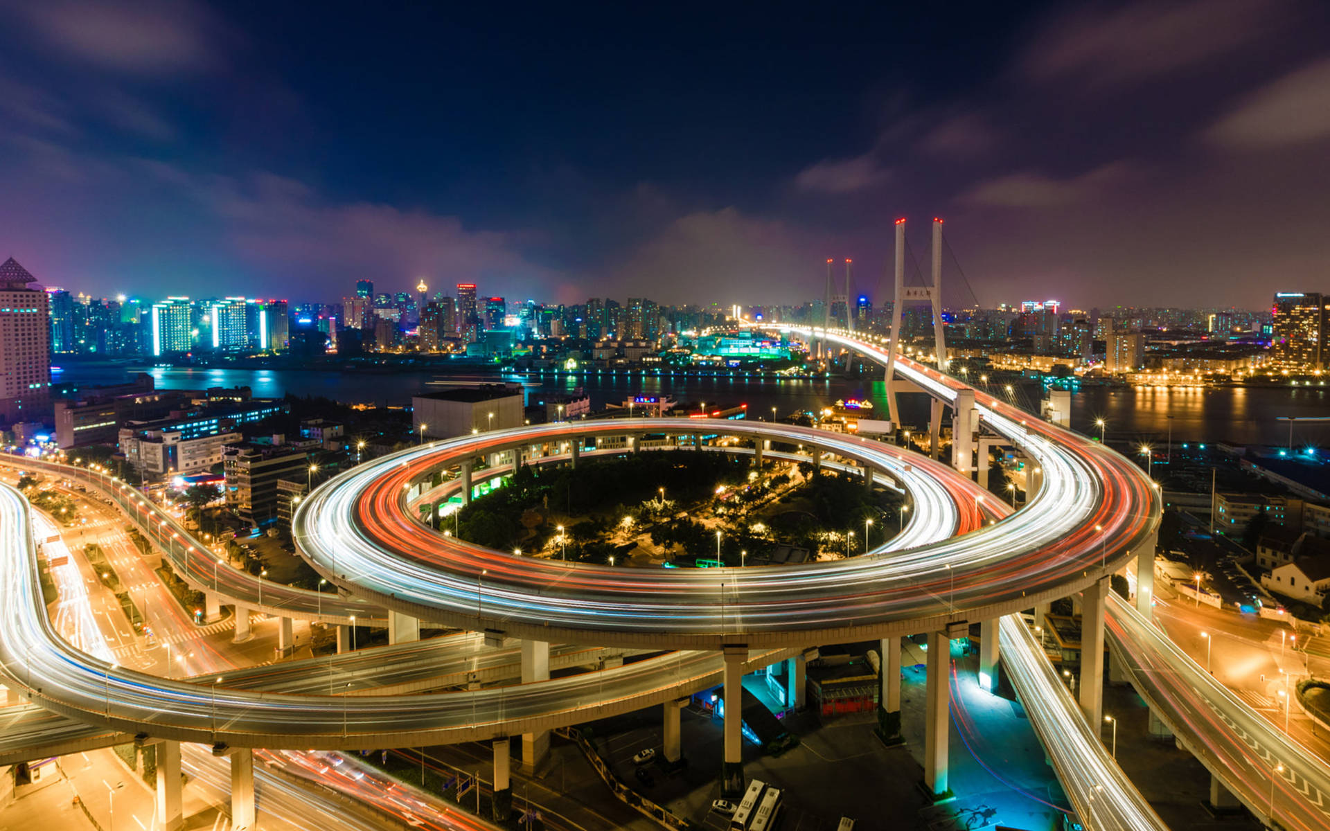 夜晚閃爍的高速公路交匯處，移動車輛的光跡和背景的城市天際線。