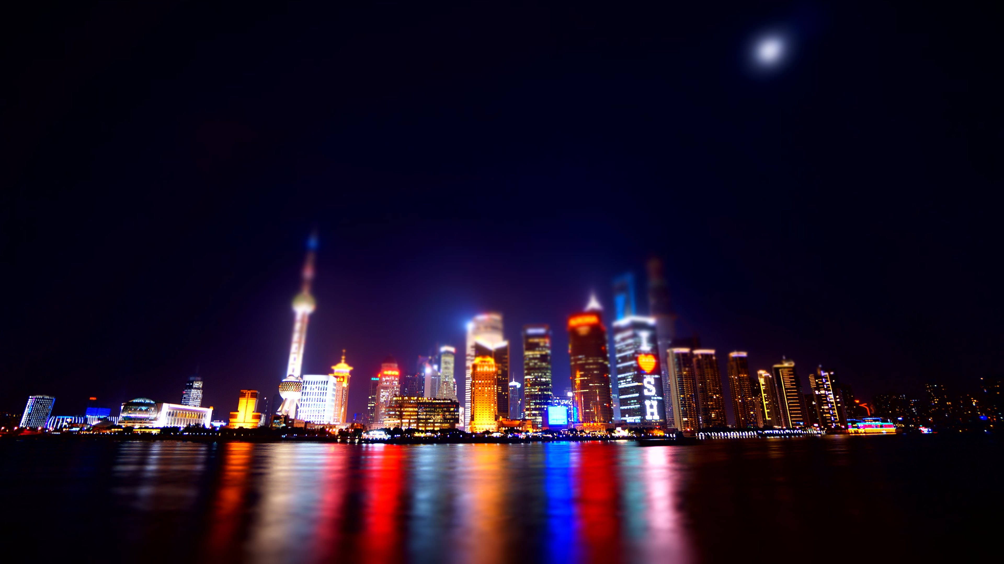 上海河畔城市 壁紙 — 充滿活力的夜景，月光下發光的摩天大樓倒映在水中。