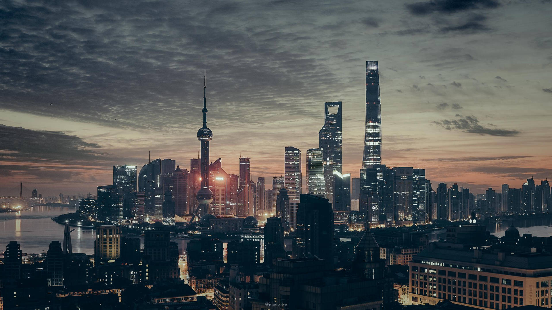 黃昏時分的上海天際線，發光的摩天大樓和下方的河流。