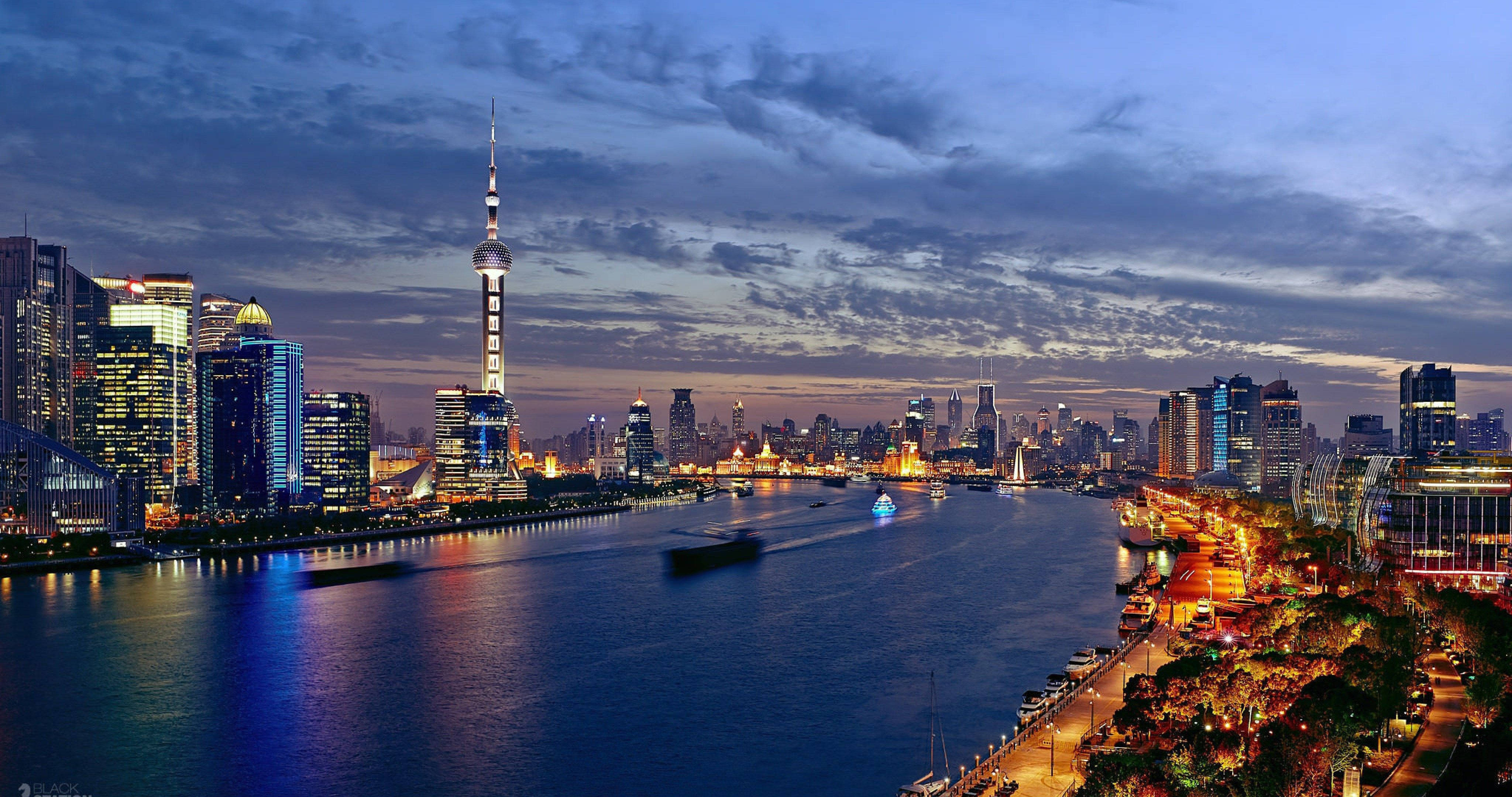 上海黃浦江畔現代都市 壁紙 — 上海黃昏時分璀璨天際線的全景，黃浦江倒映著城市燈光與往來的船隻。