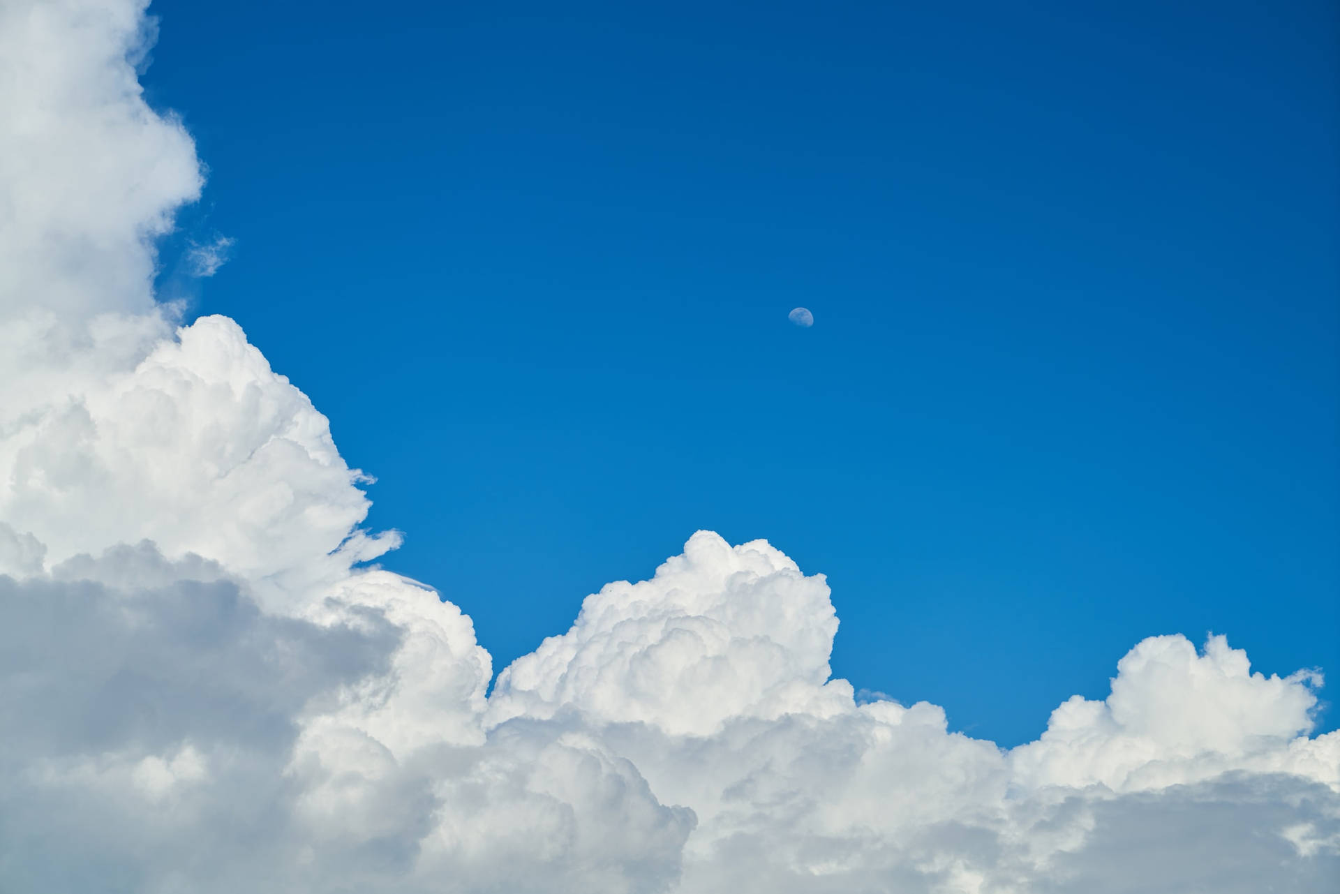 下午藍天雲層與月亮相襯 壁紙 — 廣闊的藍天充滿了蓬鬆的白雲，一彎小小的新月若隱若現。