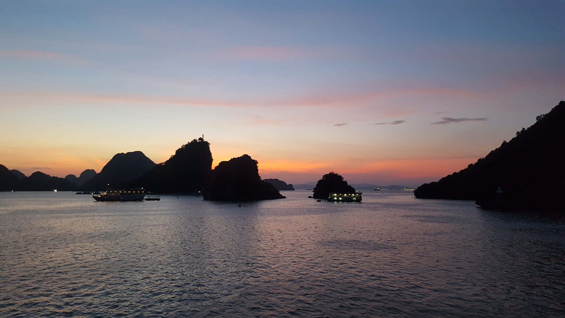 船隻在色彩繽紛的暮色天空下漂浮在黑暗島嶼附近。
