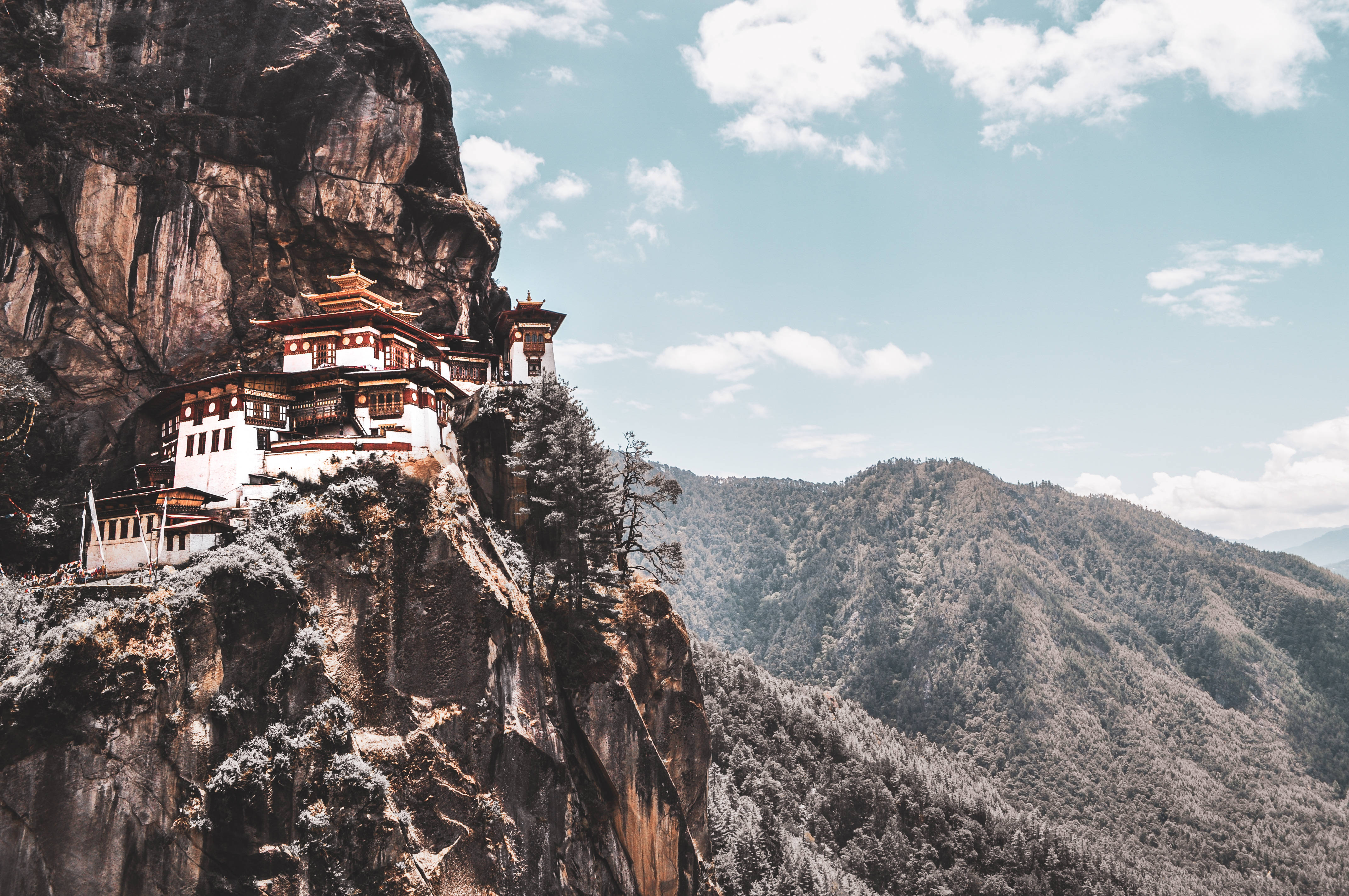 不丹佛教寺廟 壁紙 — 一座傳統佛教寺院依附在白雪覆蓋的懸崖上，俯瞰著廣闊的山谷，天空湛藍明亮。
