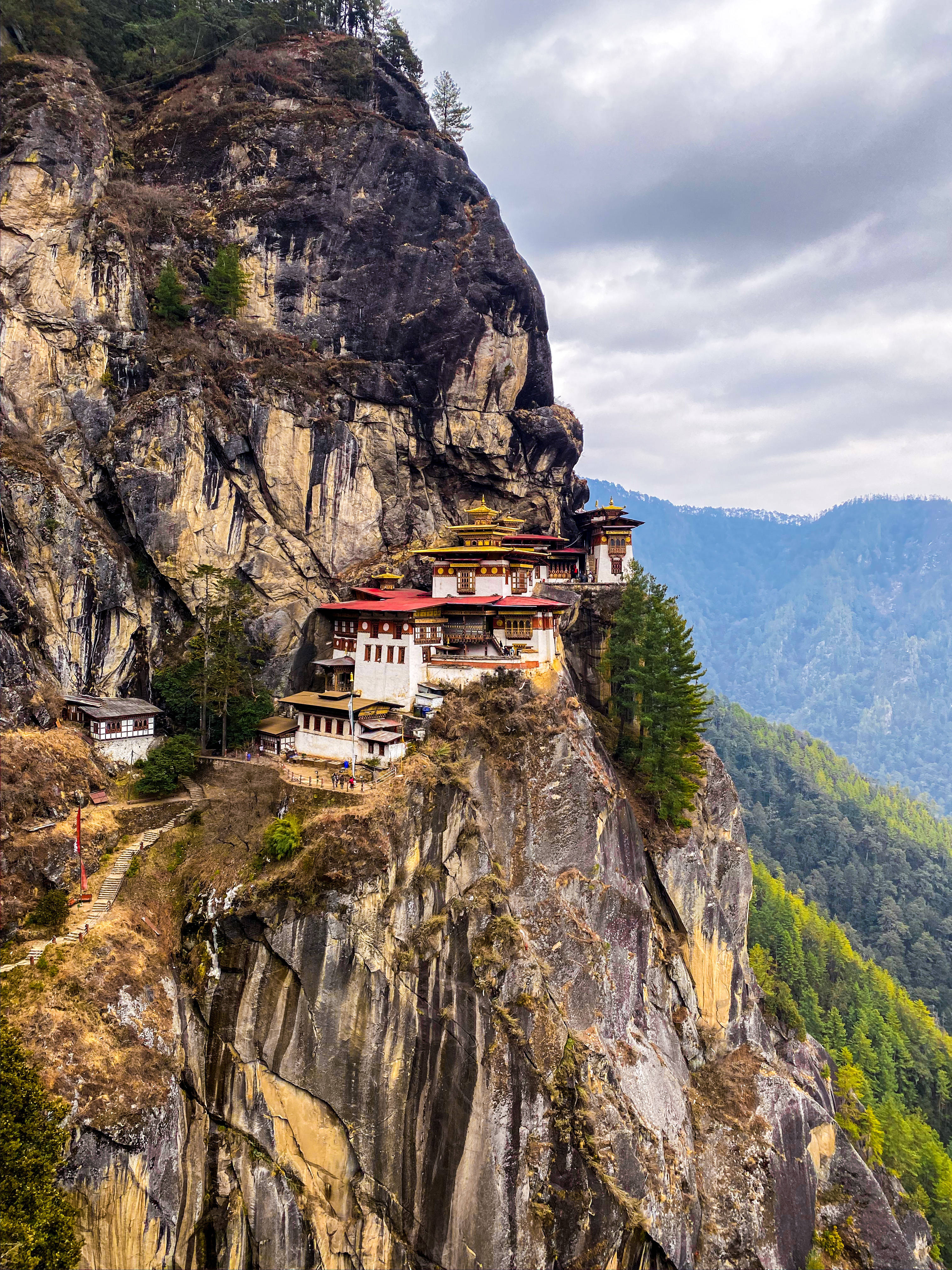 不丹懸崖寺 壁紙 — 一座令人驚嘆的修道院緊貼在陡峭的懸崖面上，俯瞰著多雲天空下廣闊的山谷。