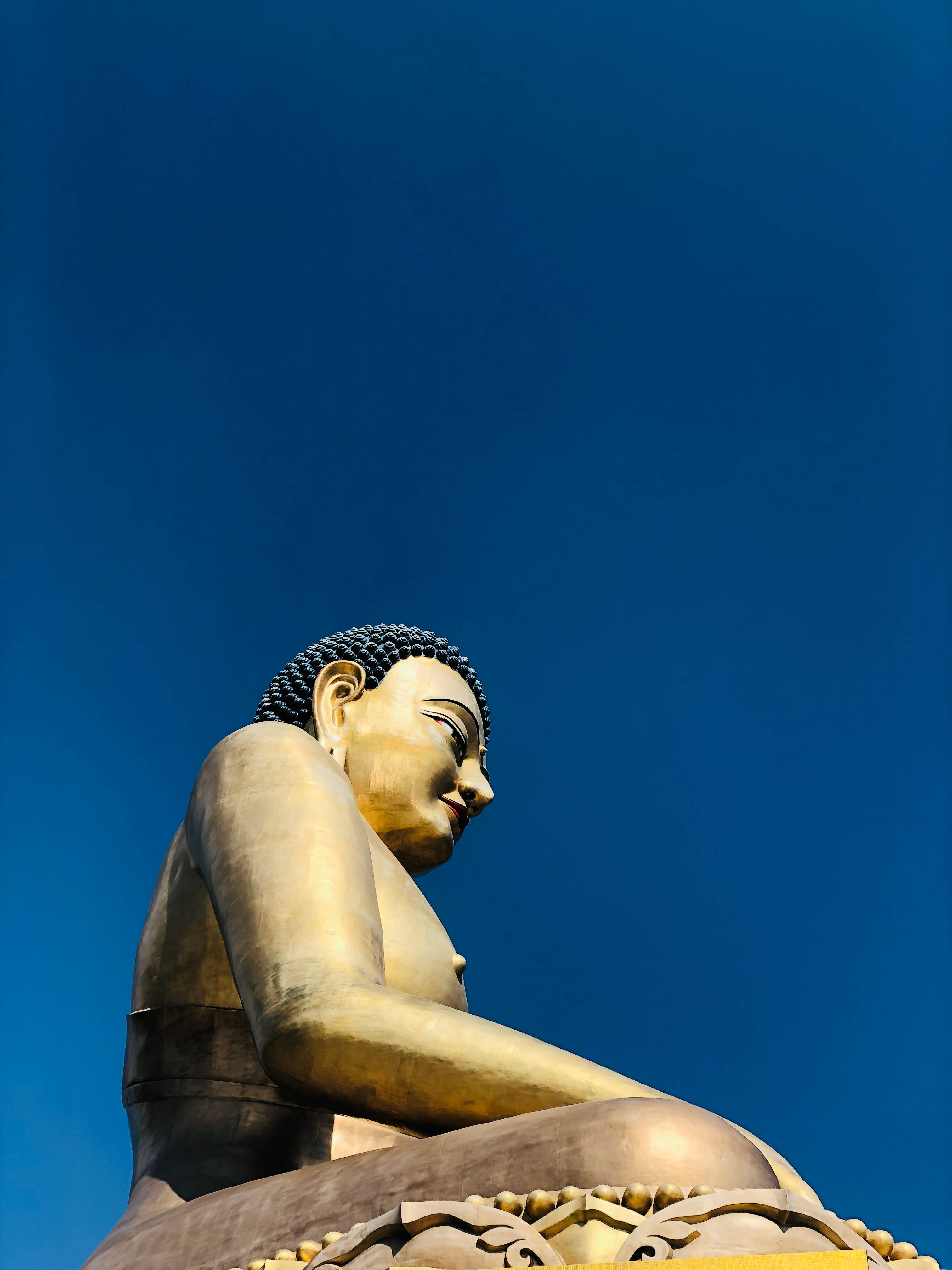 不丹金佛像 壁紙 — 一尊莊嚴的金色佛像在深藍色的天空下靜坐，散發出平靜和精神的存在。
