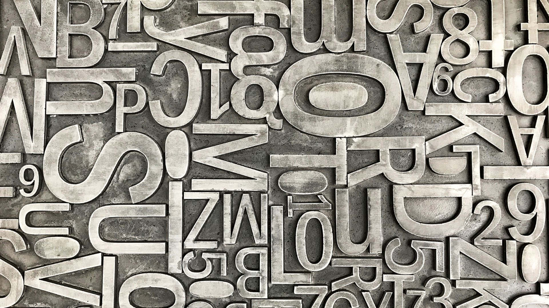 Typography 桌布 壁紙 — 不同大小和方向的金屬凸版字體密集拼砌，形成紋理豐富的工業風格字體牆。