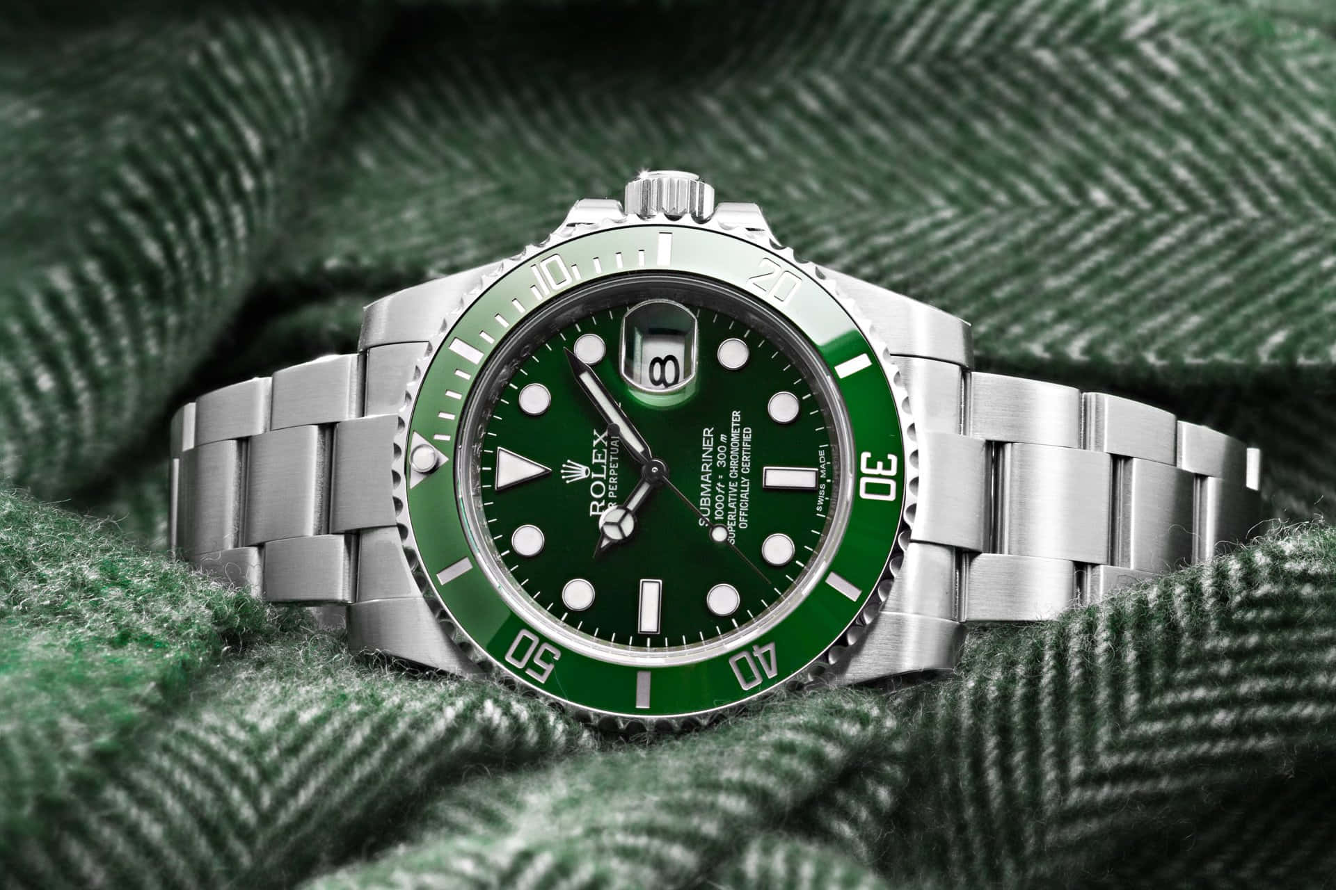 Rolex 桌布 壁紙 — 不鏽鋼勞力士潛航者型腕錶，配以充滿活力的綠色錶盤，優雅地放置在帶有紋理的綠色人字紋布料上。
