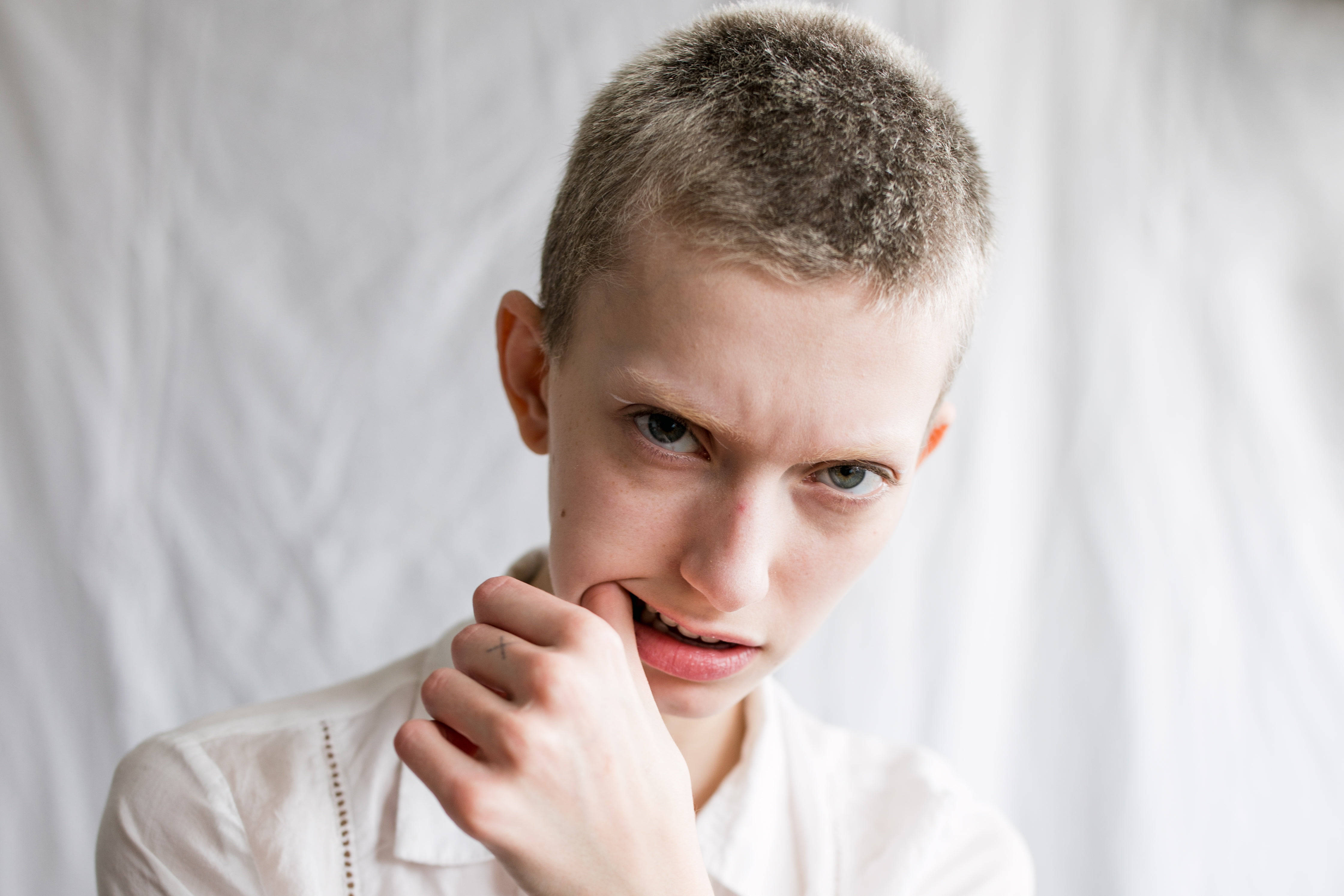 不開心生氣男孩 壁紙 — 一位短灰髮的人士在白色背景下咬著嘴唇，專注地凝視鏡頭。
