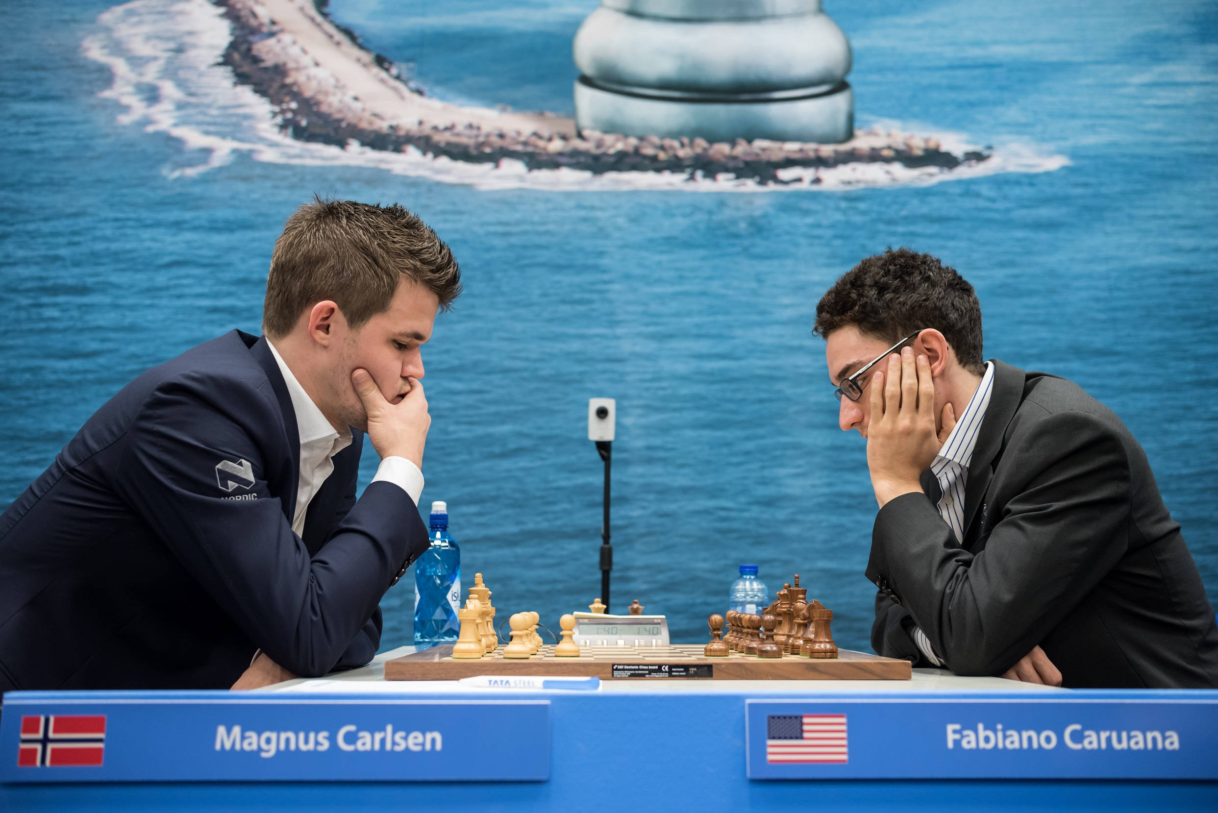 世界國際象棋冠軍馬格努斯·卡爾森與法比亞諾·卡魯阿納深思對弈 壁紙 — 兩位國際象棋大師在海岸背景下進行高風險比賽時高度專注。