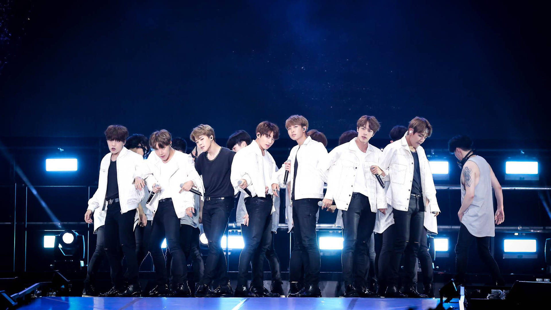 世界巡迴酷炫BTS筆電壁紙 壁紙 — 一個K-pop組合在黑暗舞台上充滿活力地表演，舞台被明亮的藍色聚光燈和煙霧效果照亮。