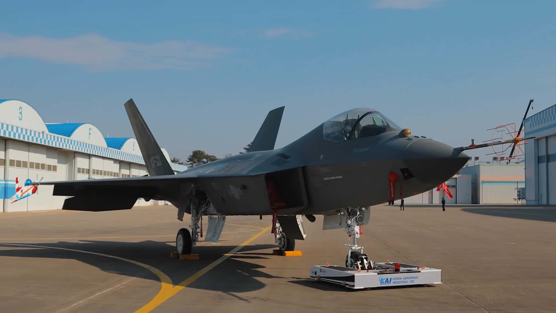 灰色戰鬥機停在機場停機坪，靠近機庫，藍天背景