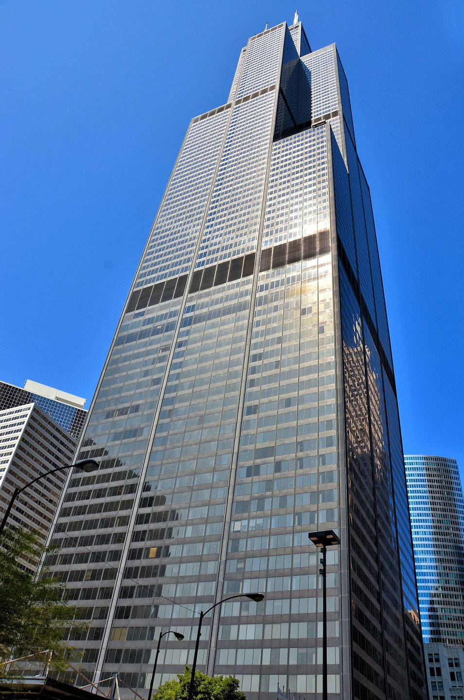 世界最高建築威利斯大廈 壁紙 — 一座高聳的玻璃摩天大樓以其反射外牆映照周圍建築物和陽光，刺破清澈的藍天。