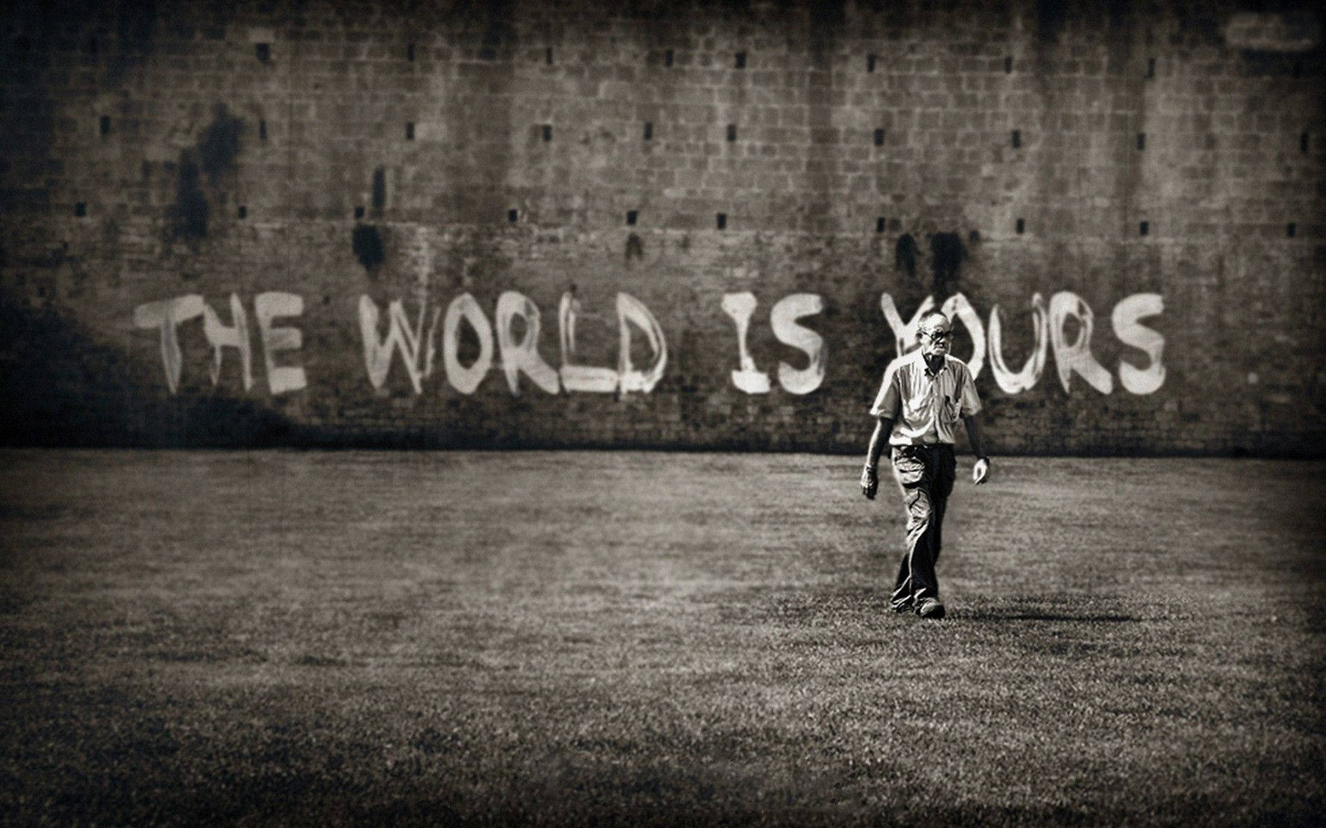 男人在塗鴉牆下走向觀眾，牆上寫著「The World Is Yours」