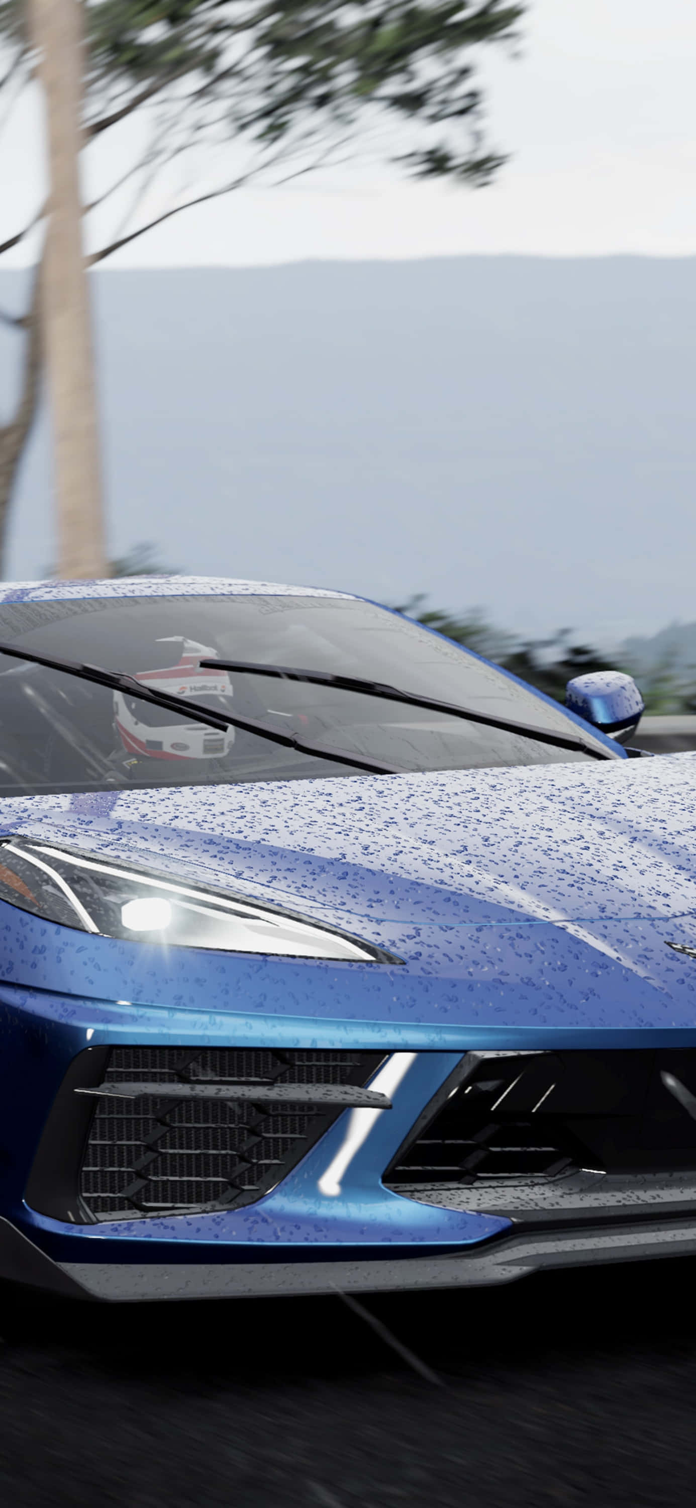 世界知名賽車遊戲《Project Cars 2》的精彩畫面 壁紙 — 一輛藍色跑車引擎蓋上有雨滴，在濕滑的道路上疾馳，背景是山脈。