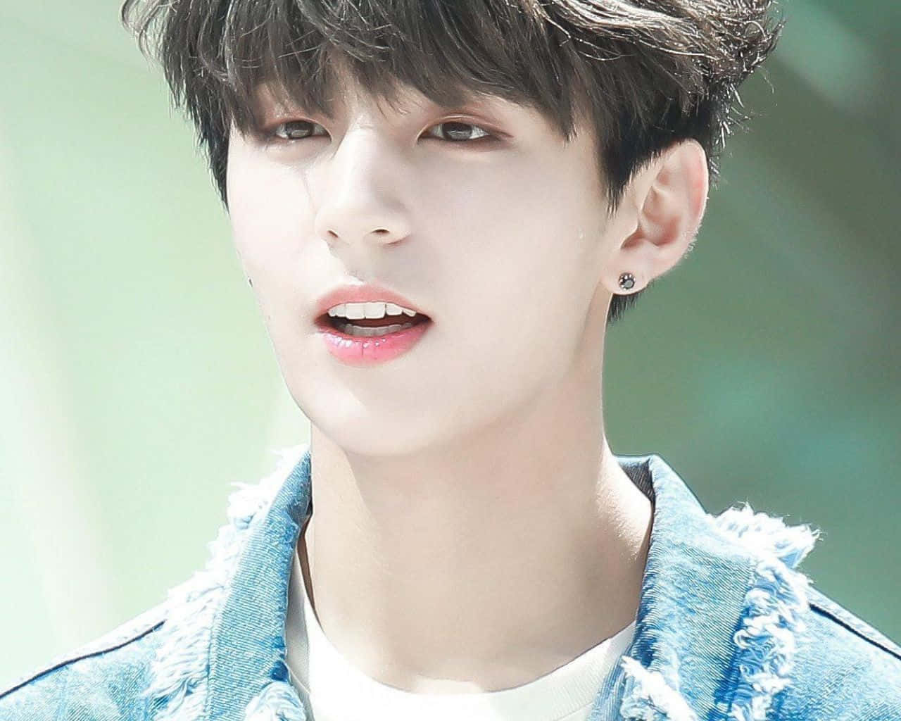 世界聞名的BTS成員Jungkook凝望遠方 壁紙 — 一個黑髮、身穿牛仔褸的年輕男子，在模糊的綠色背景下，帶著柔和的表情向上望。