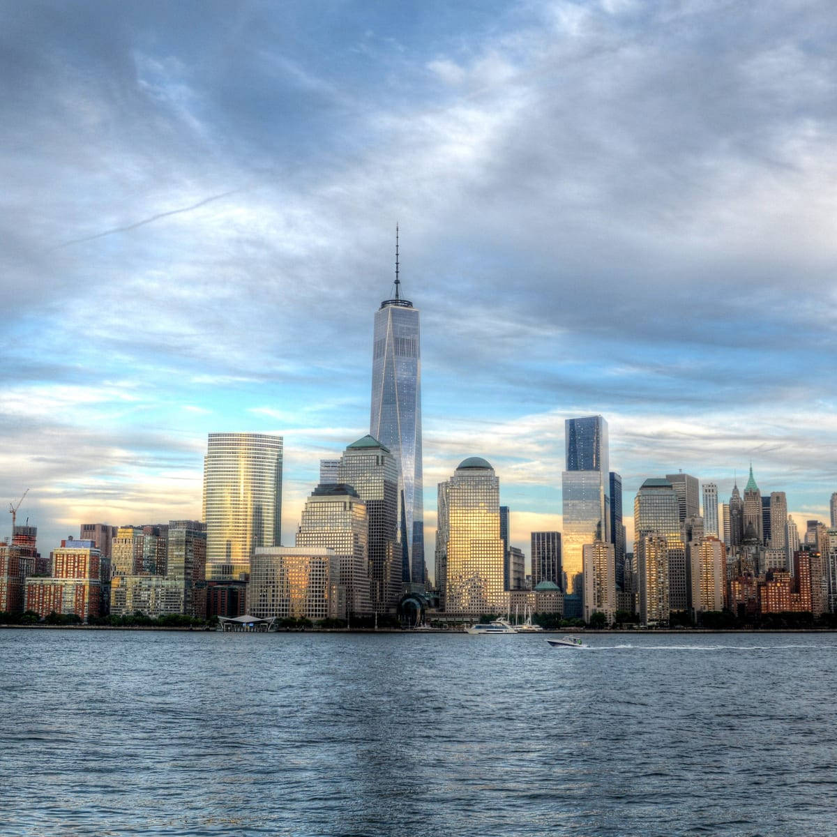 日落時分的紐約市天際線，One World Trade Center 和水面上的船隻。