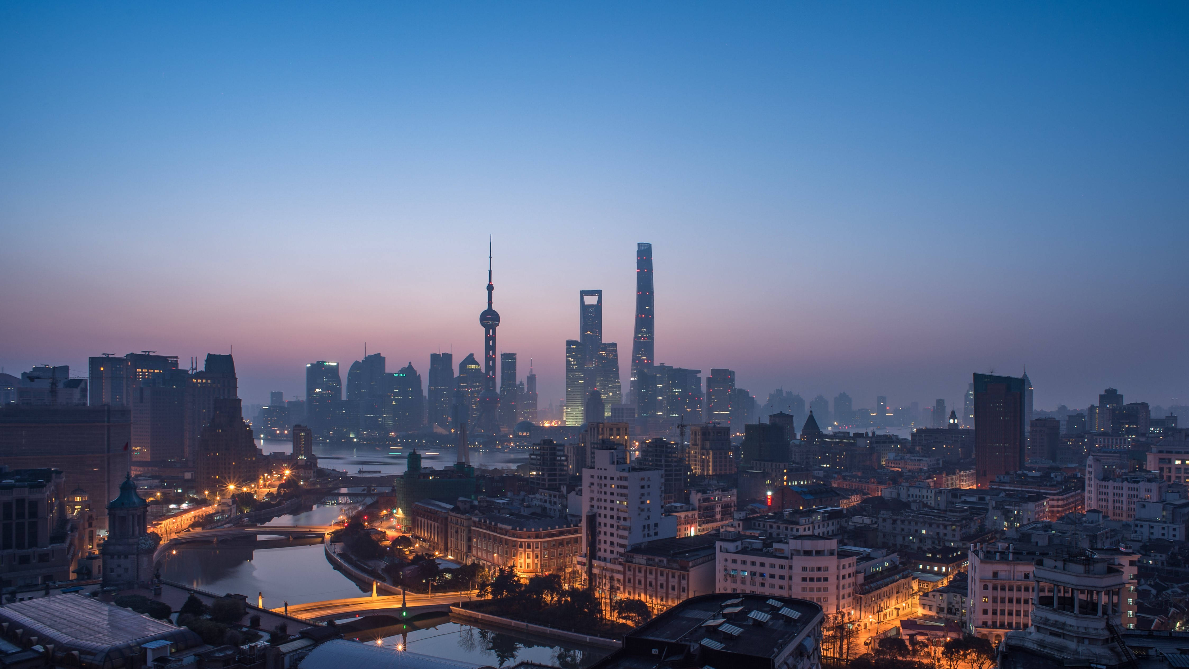 中國上海城市夜景 壁紙 — 上海天際線的黃昏全景，高樓大廈燈火通明，河流蜿蜒穿過城市。