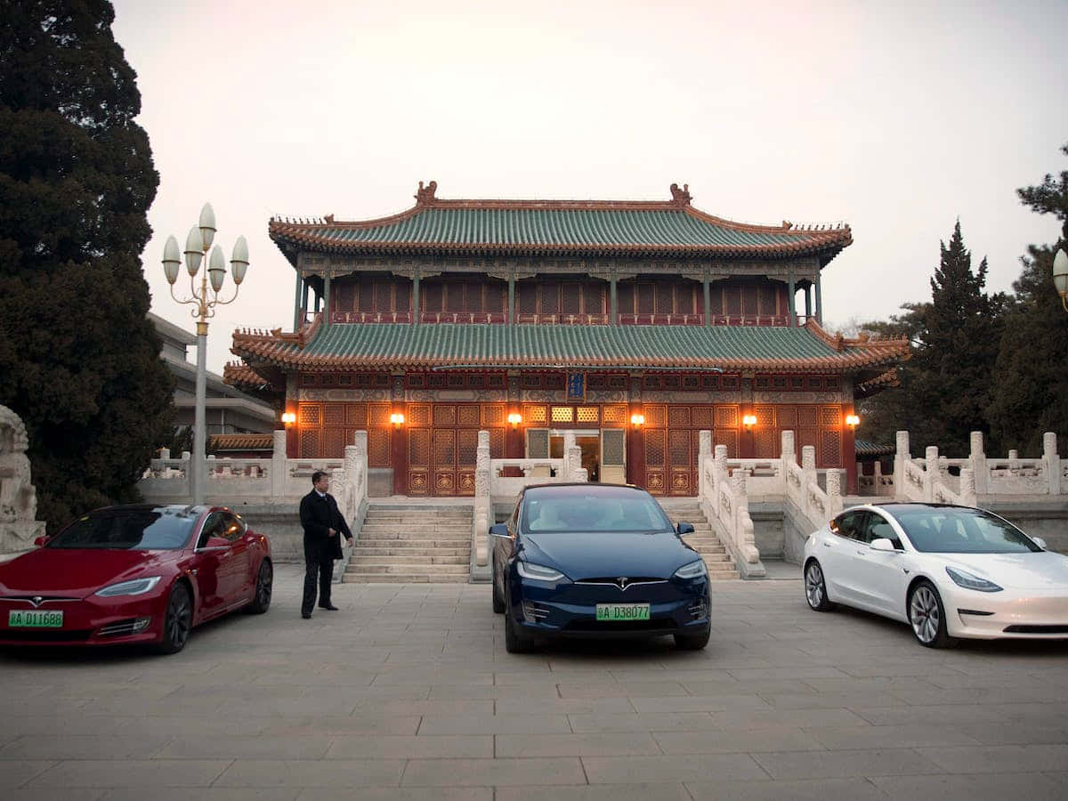 中國之美 壁紙 — 三輛Tesla汽車停在一座傳統中國寺廟前，溫暖的燈光在黃昏中閃爍。