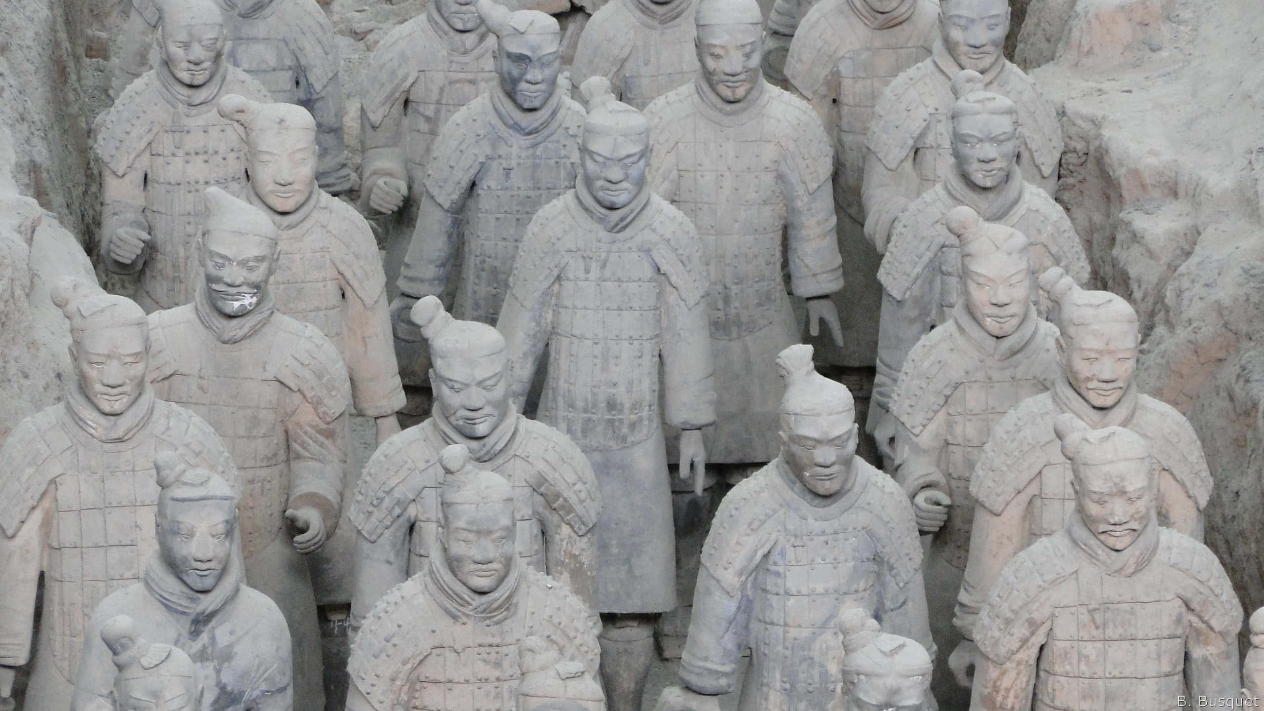 中國博物館內的歷史秦俑雕塑 壁紙 — 一排排古老的兵馬俑以大地色調站立，帶有精細的盔甲和莊嚴的表情。