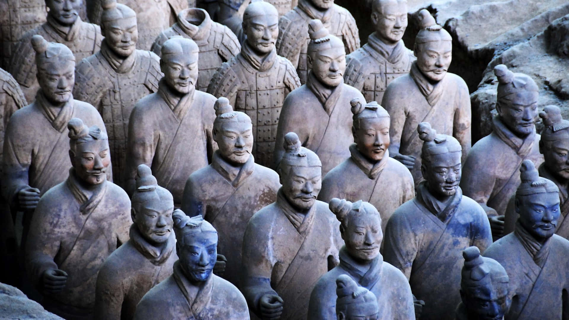 中國博物館灰陶俑雕塑 壁紙 — 一排排古老的兵馬俑莊嚴地矗立在地下坑道中，呈現泥土色調和精細的盔甲。