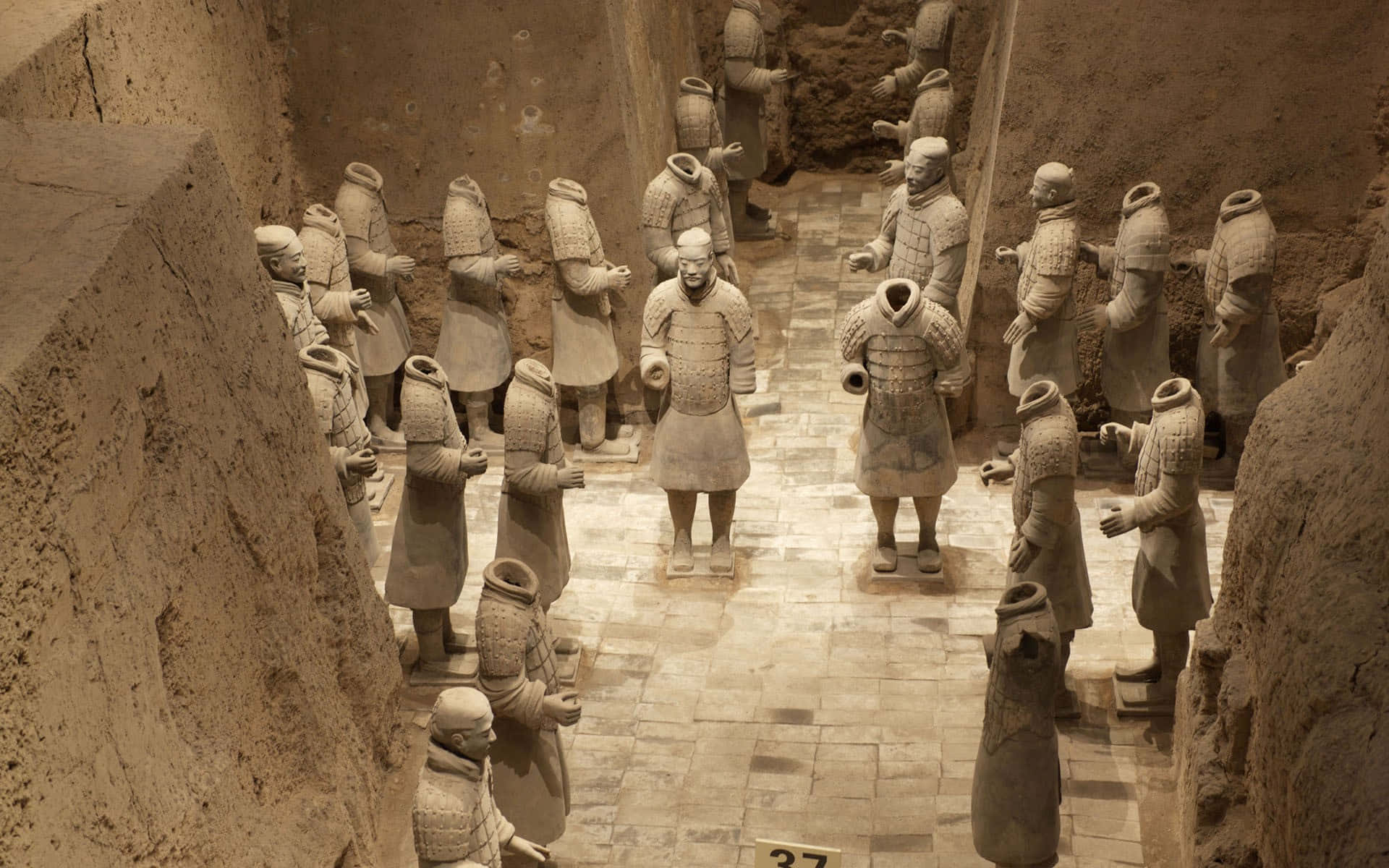 中國博物館陶俑雕塑 壁紙 — 一排排古老的兵馬俑在泥土色的發掘室內列隊站立。