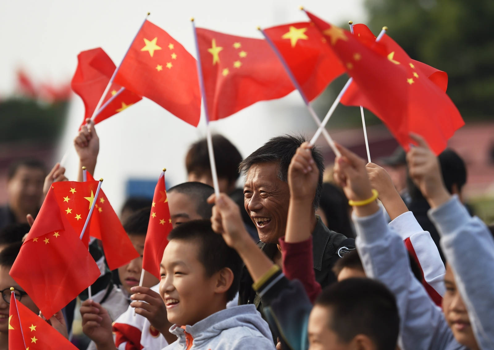 中國國旗微笑 壁紙 — 一群歡樂的人們在明亮的日光下揮舞著帶有黃色星星的紅色中國國旗。