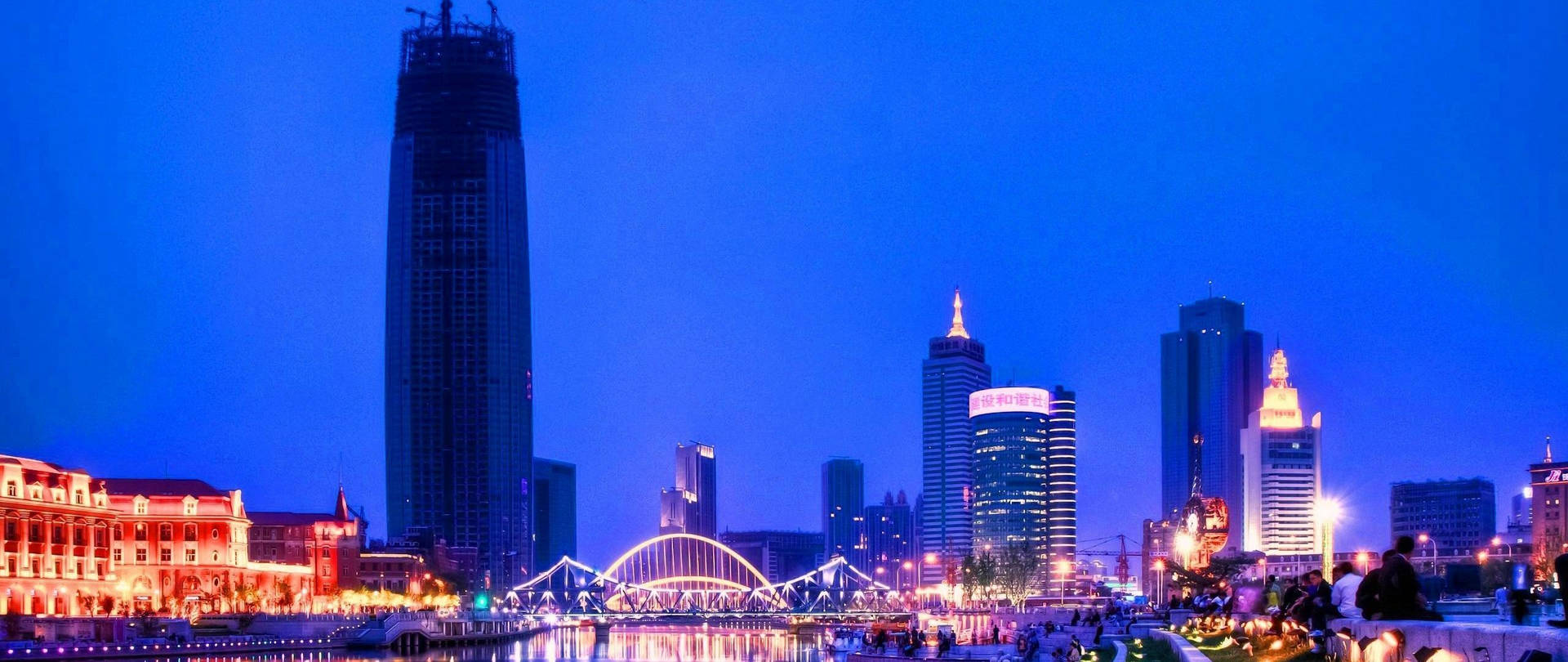 黃昏時分的城市天際線，明亮的建築物和水面上的橋樑
