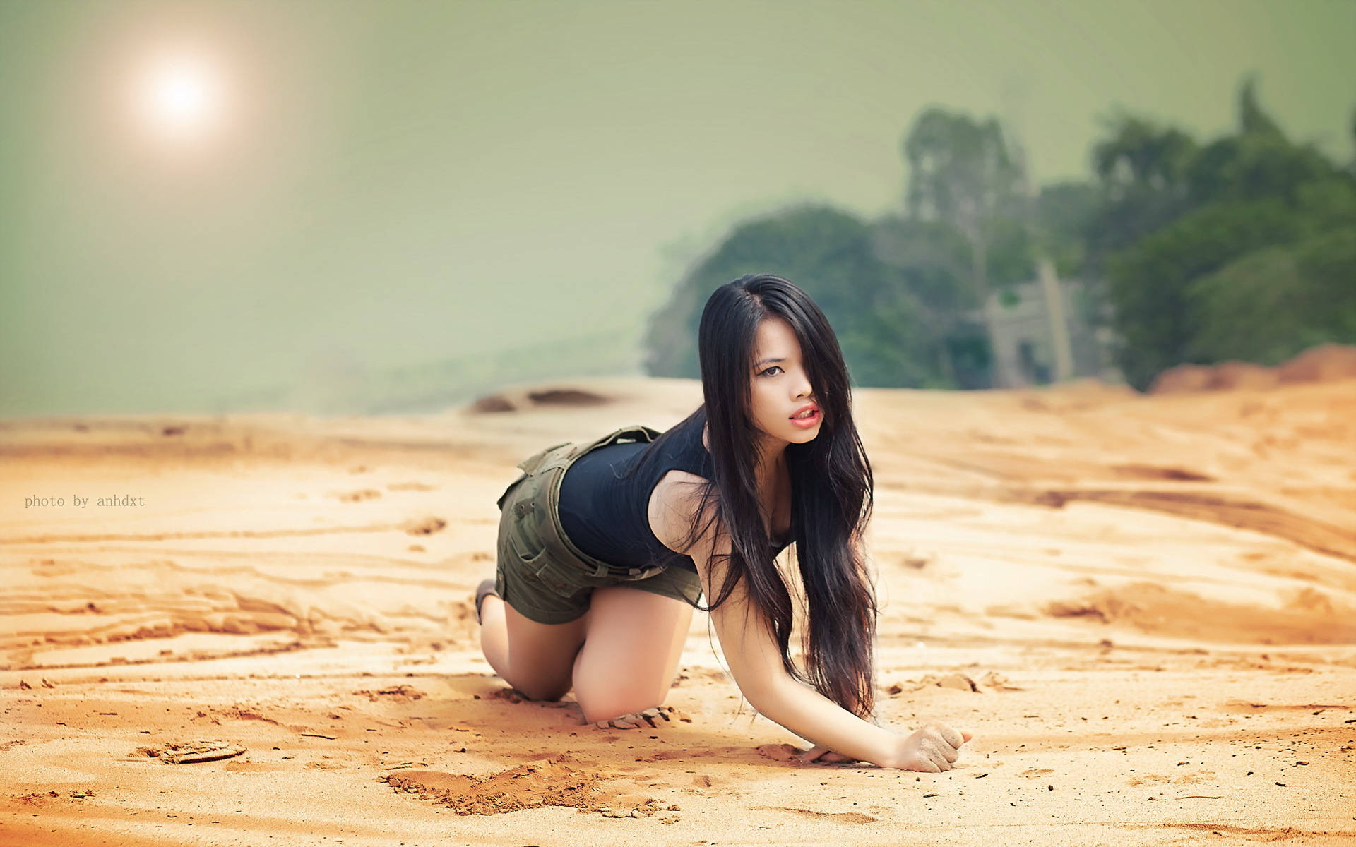 女子在明亮陽光下跪在沙上看著觀者