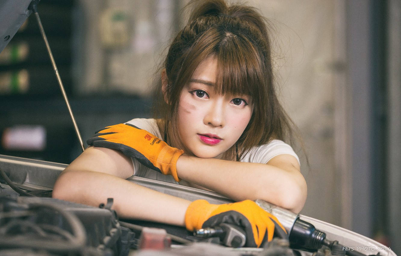 年輕女機械師戴橙色手套將手臂擱在汽車引擎蓋上