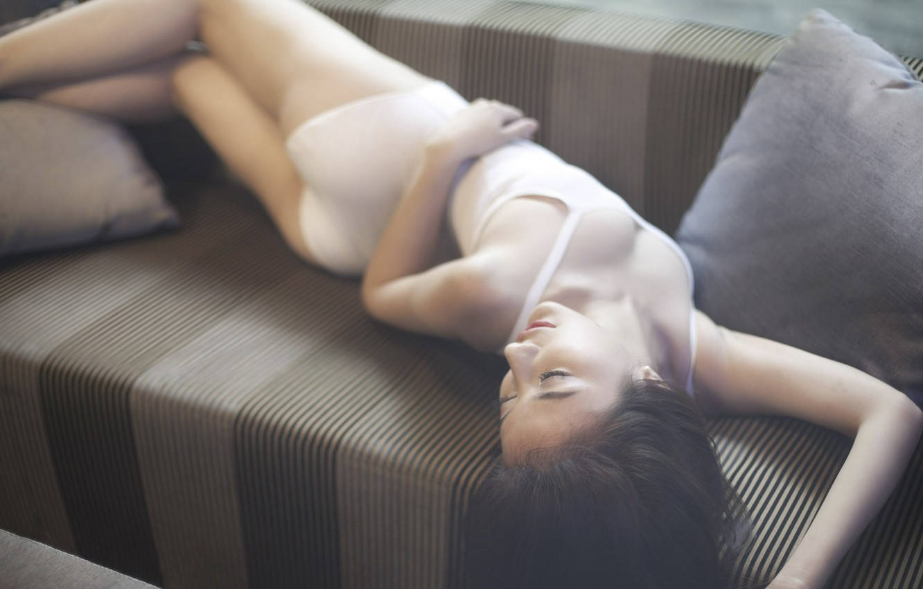 一位身穿白色內衣的女性靠在帶有枕頭的條紋沙發上。