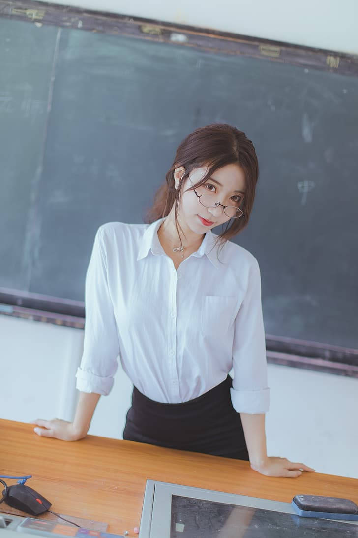戴眼鏡、穿白色襯衫的年輕女子靠在教室的桌子上