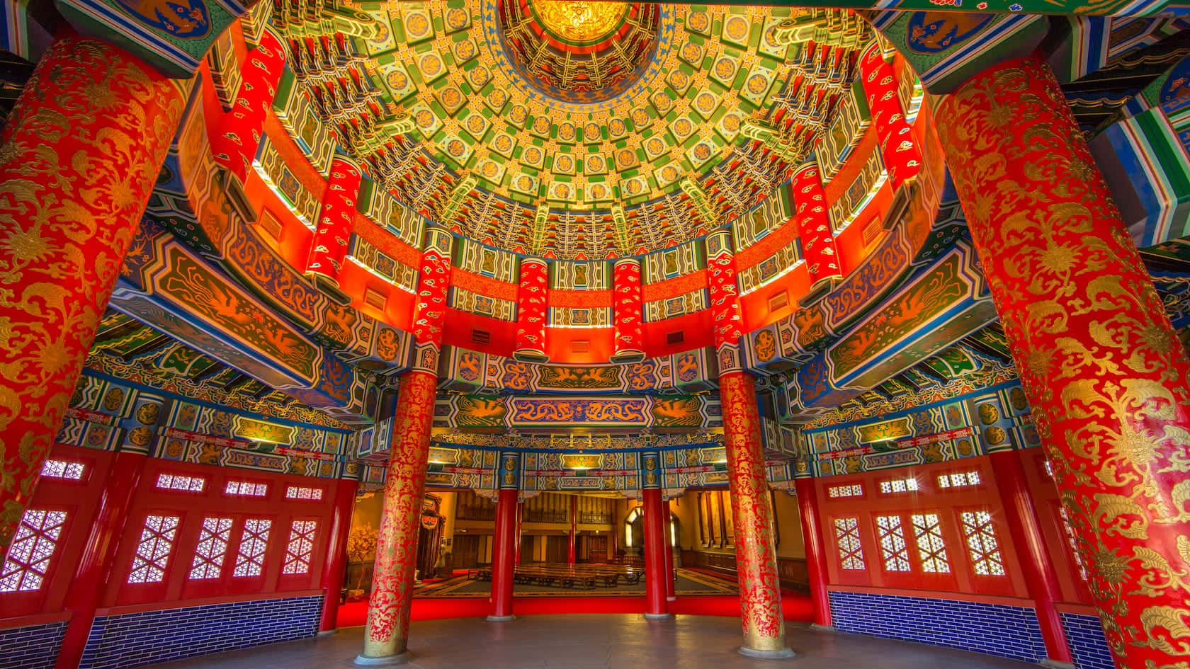 中國張家界附近山巒與薄霧的壯麗景色 壁紙 — 宏偉華麗的寺廟內部，擁有高聳的紅色柱子、金色鏤雕，以及裝飾著複雜圖案和溫暖燈光的耀眼多層天花板。
