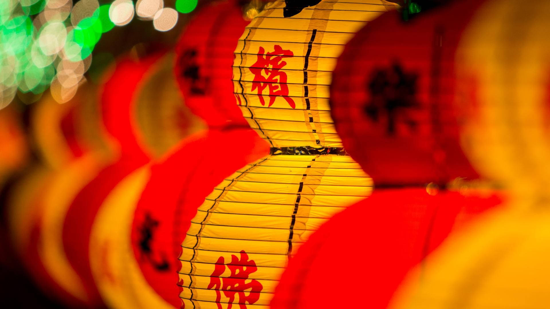 中國新年傳統燈籠 壁紙 — 鮮豔的紅色和黃色紙燈籠上帶有發光的中文字，掛在綠色和白色燈光的散景背景前，形成一排節日裝飾。