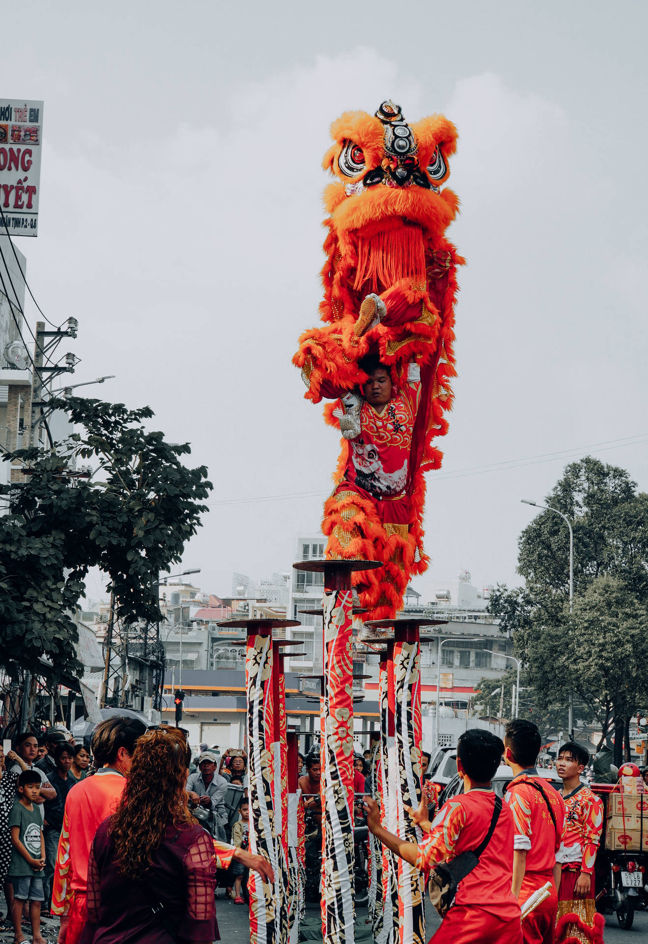 穿著紅色服裝的表演者在街頭慶祝活動中，在高桿上平衡一個大型橙色舞獅木偶。