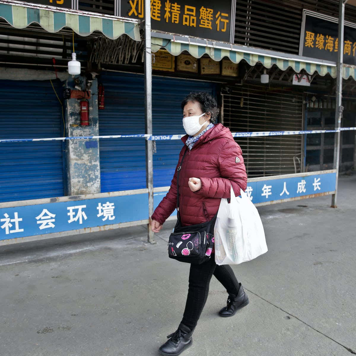 中國桂林附近河流與山脈的黑白航拍美景 壁紙 — 一名身穿栗色羽絨外套和口罩的女子走過被警方封條封鎖的關閉店舖。