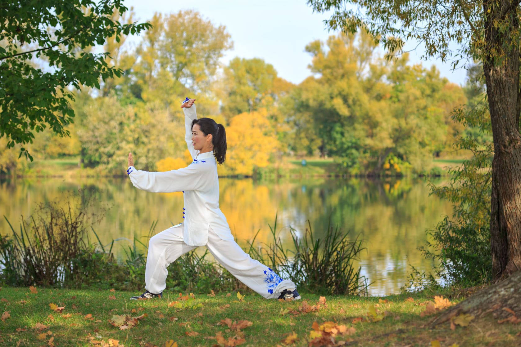 女子在秋湖邊練習太極拳。