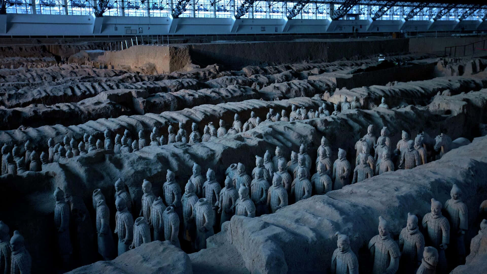 中國秦始皇陵兵馬俑巨型展廳 壁紙 — 一排排古老的兵馬俑在現代保護屋頂下，於其龐大的考古發掘現場中列隊站立。