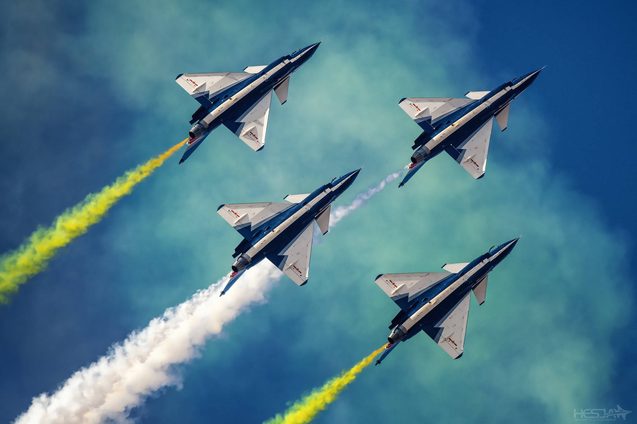 中國空軍表演 壁紙 — 四架戰鬥機在鮮豔的藍天中緊密編隊飛行，留下鮮明的黃色和白色煙跡。
