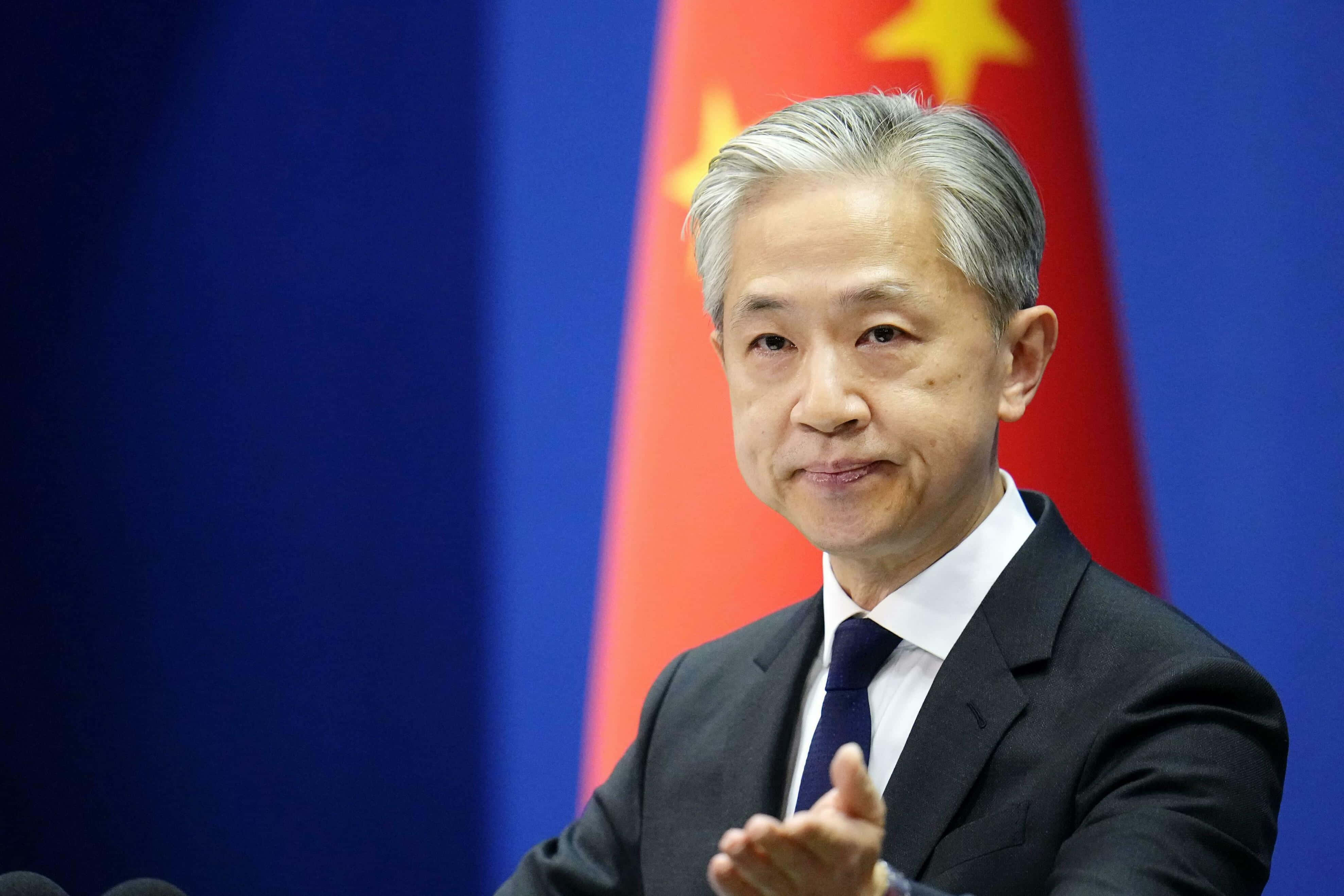 中國蓮花池上的木橋 壁紙 — 一名身穿深色西裝的男子在記者會上發言時做手勢，身後有中國國旗。