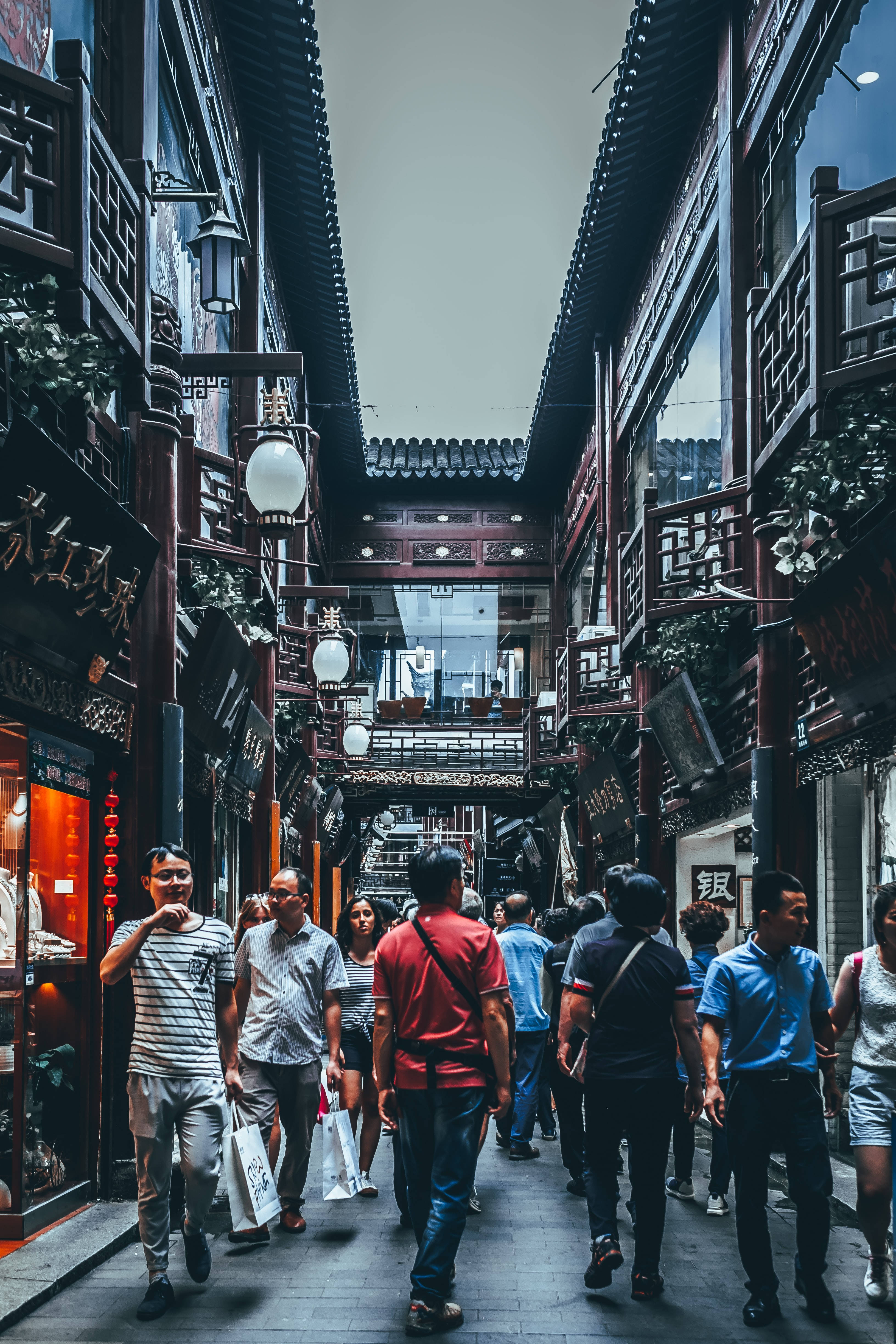 中國街巷行人 壁紙 — 一條熱鬧的狹窄小巷，兩旁是傳統中式建築，行人走在華麗的木製陽台下。