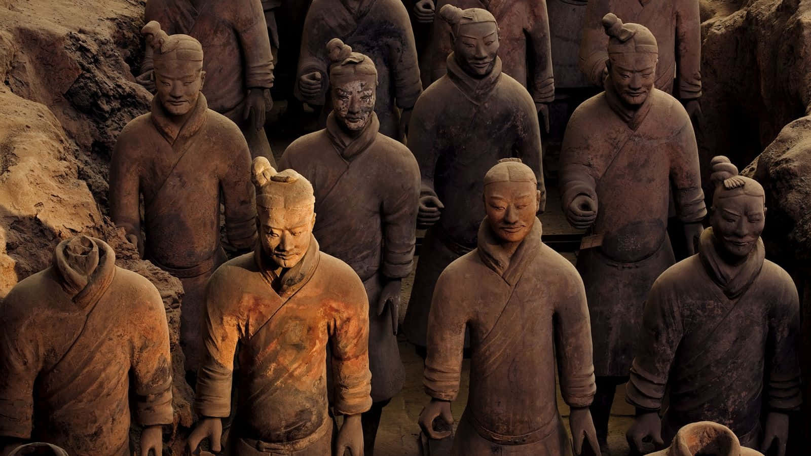 中國西安秦始皇陵陶俑軍隊 壁紙 — 一排排古老的兵馬俑莊嚴地站立在泥土的墓坑中，帶有細緻的面部表情和風化的陶土紋理。