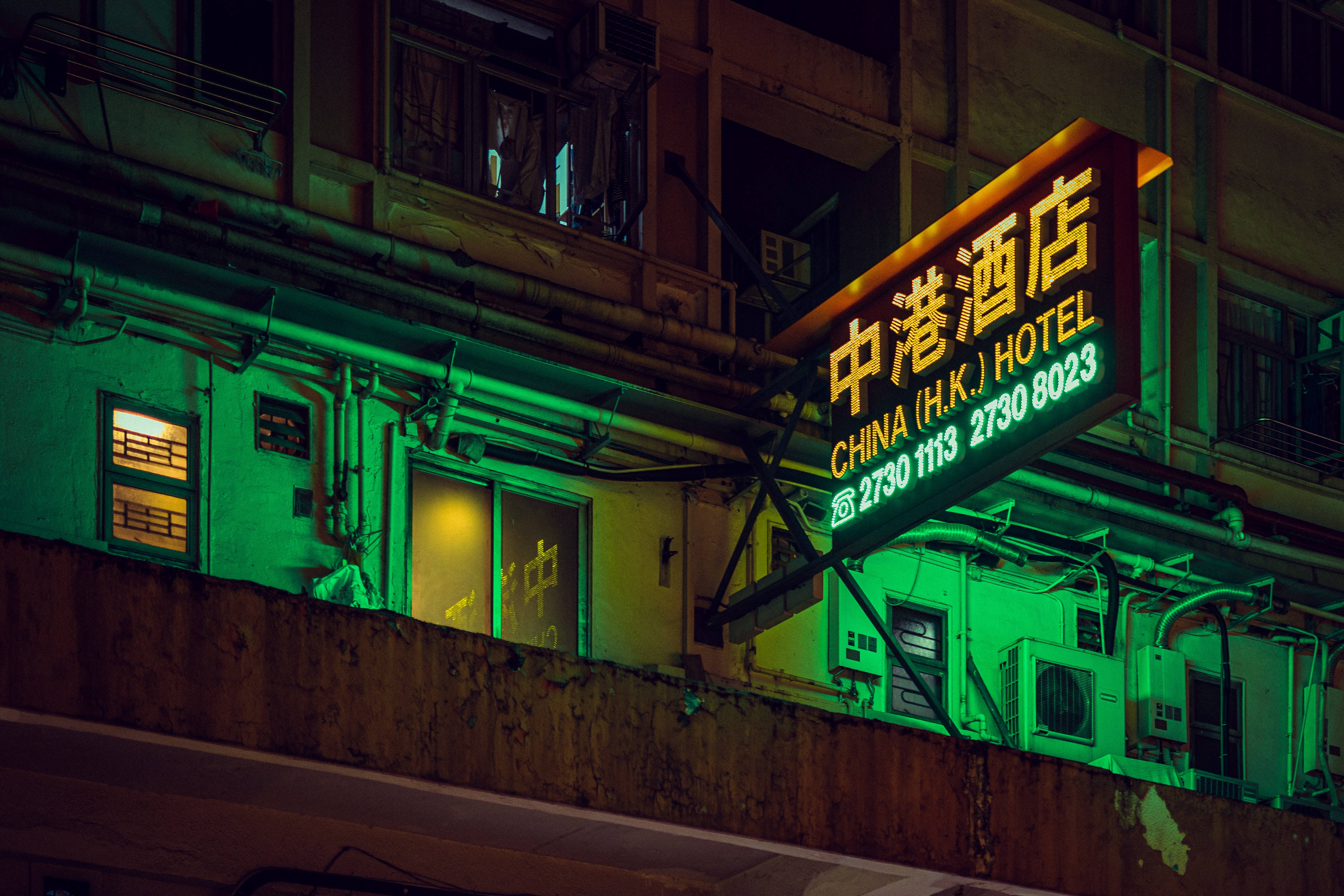 中國酒店霓虹招牌 壁紙 — 中國香港酒店閃爍的霓虹燈招牌在夜晚將鮮豔的綠光投射在風化的城市建築上。