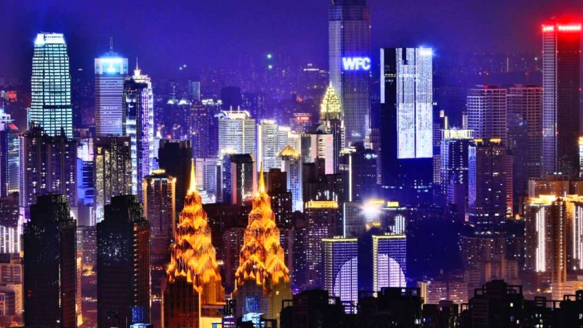 中國重慶：炫目夜景 壁紙 — 一個令人眼花繚亂的夜景城市景觀，高聳的摩天大樓在黑暗的天空中閃爍著鮮豔的藍色、紫色和金色。